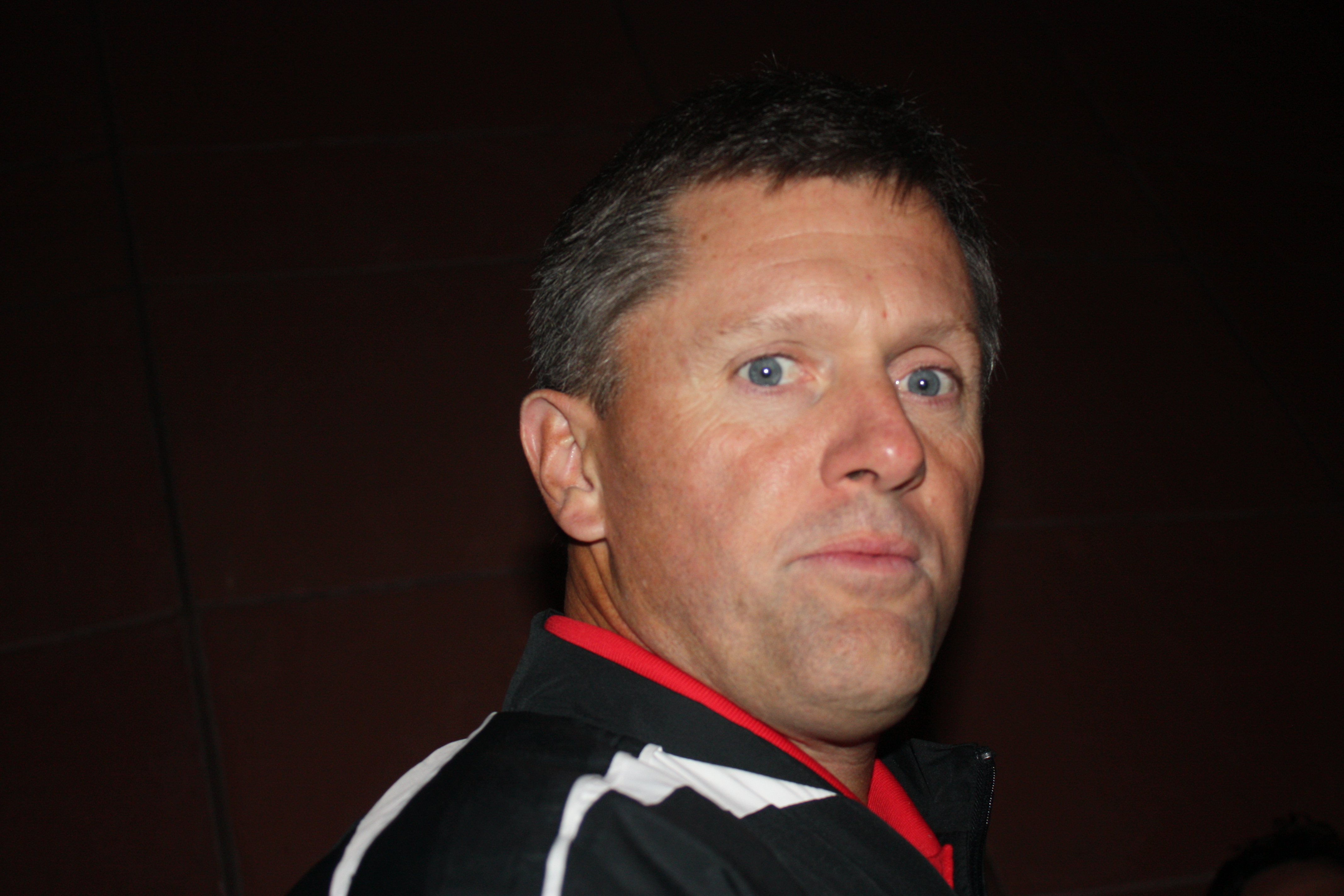 Man in black and red athletic jacket looks over his shoulder toward the camera.