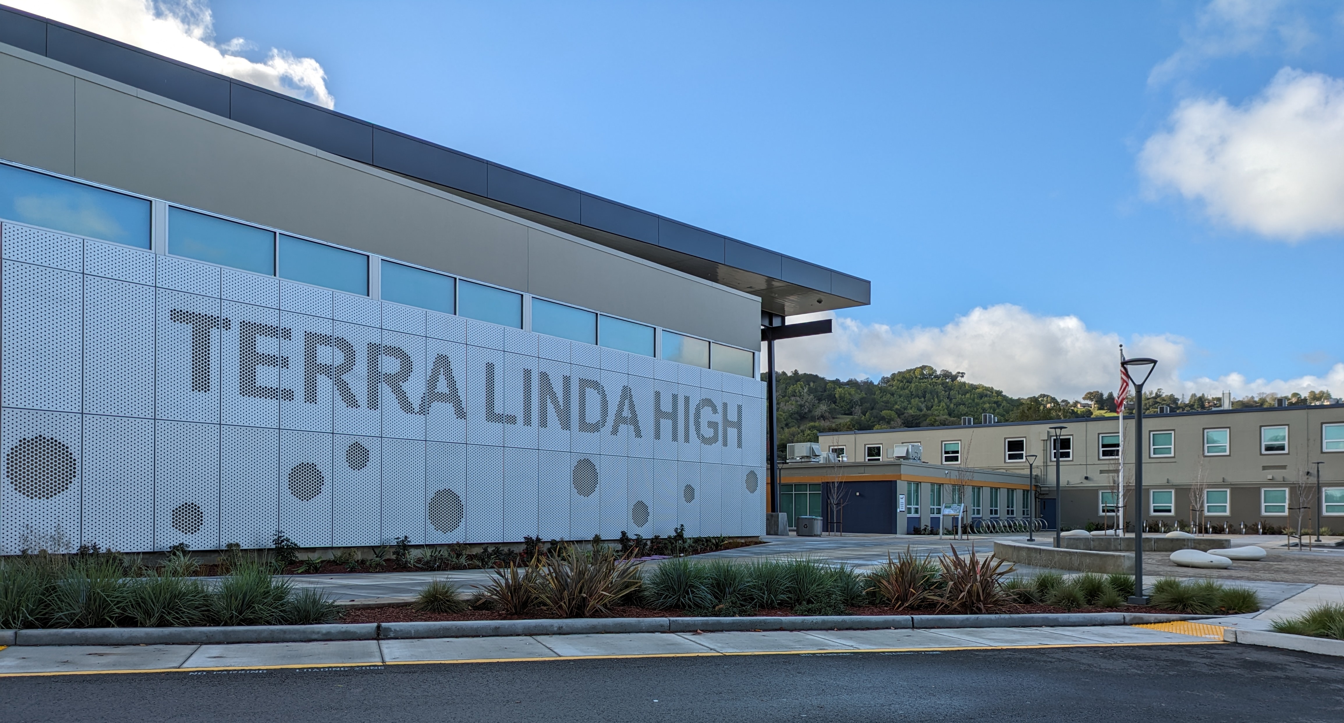 Modern school building exterior with large lettering on a white panel wall and landscaping in front.