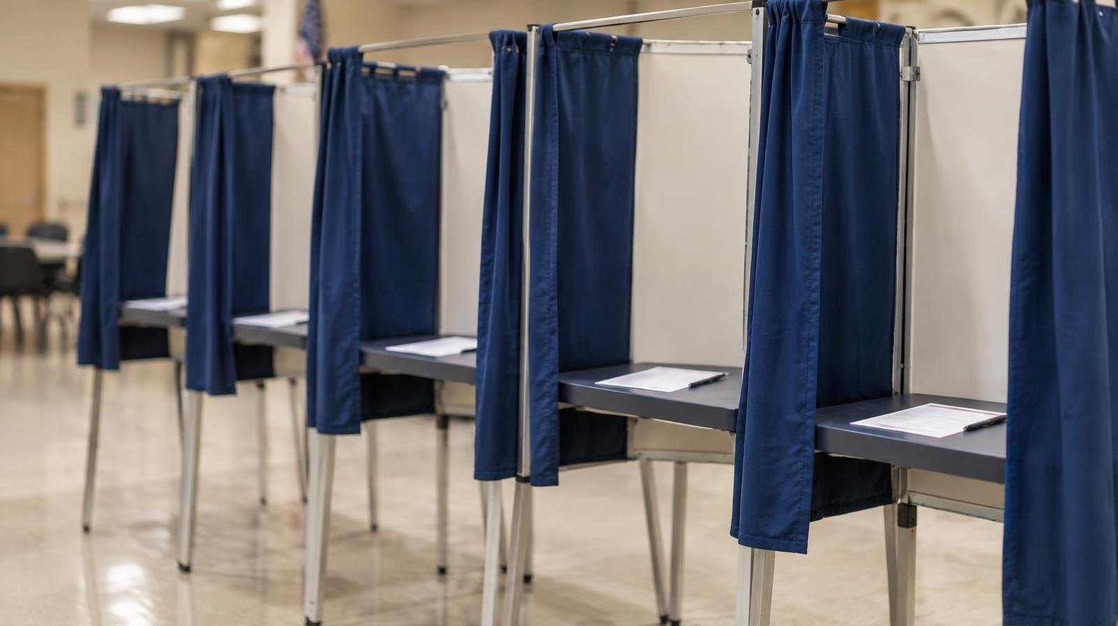A row of five voting booths with privacy curtains in a polling place.