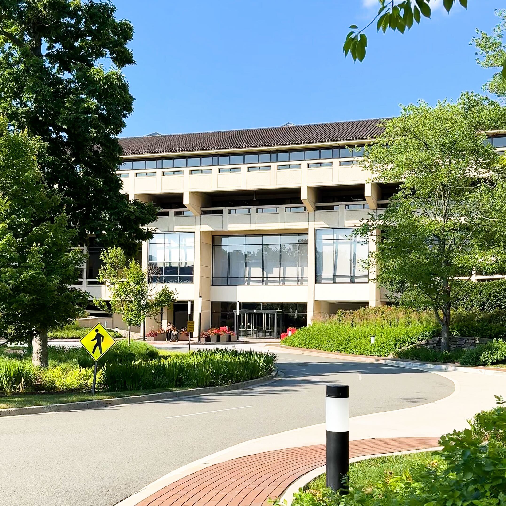 Glass-fronted corporate office building with manicured trees and a curved brick driveway.