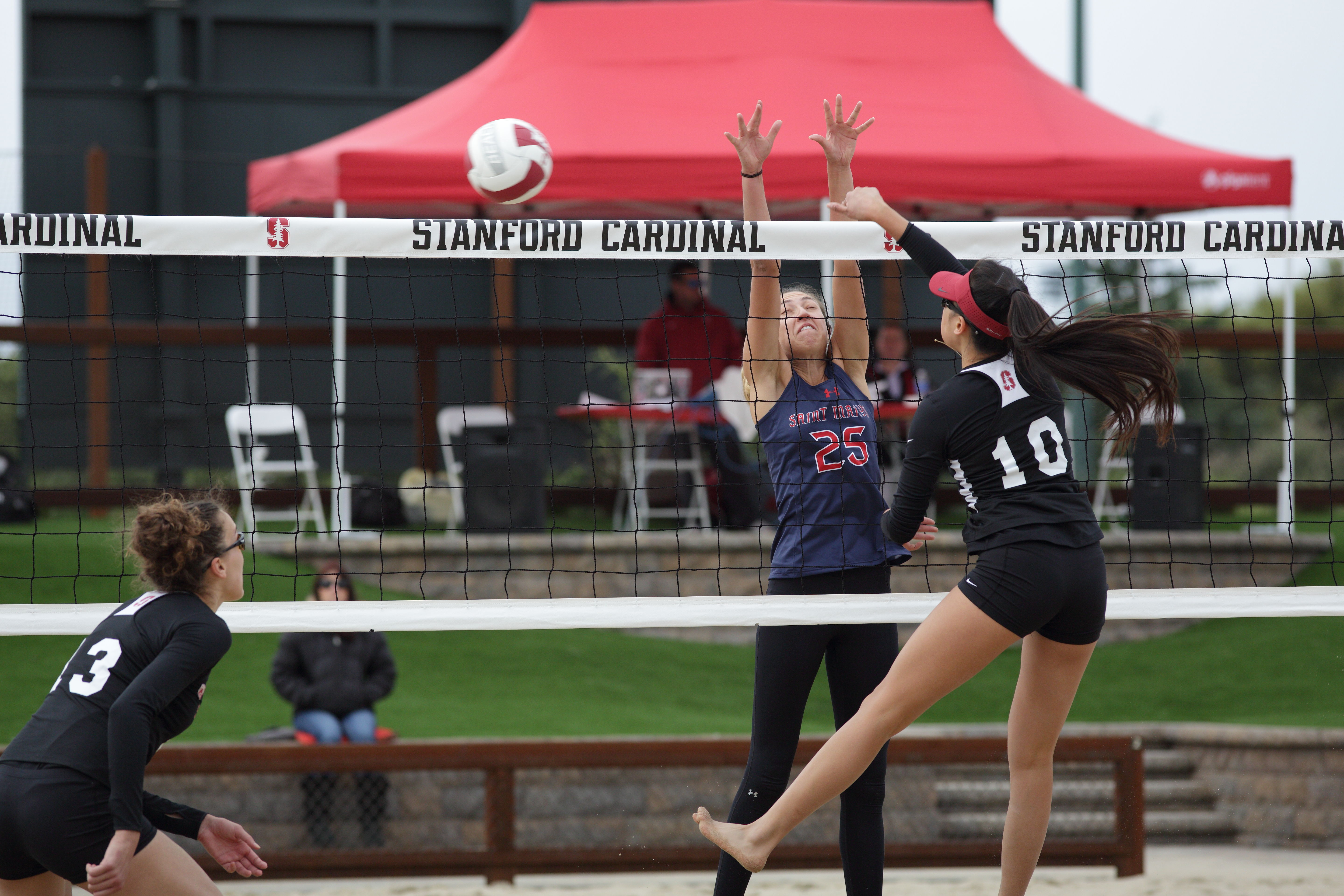 Two female volleyball players compete at the net, one spiking and one blocking.