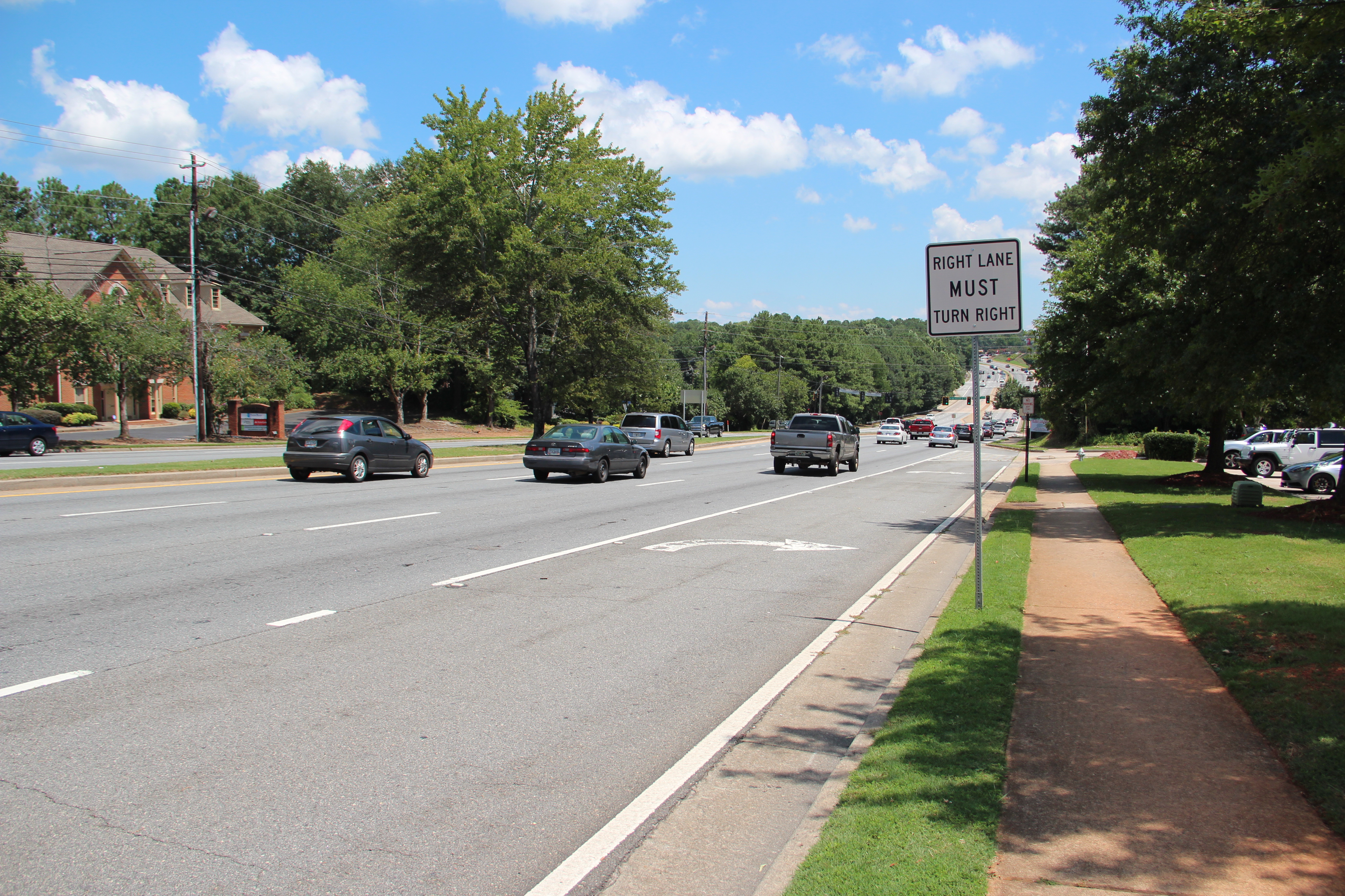 Multi-lane road with moving vehicles, a right-turn sign, and tree-lined sidewalk.