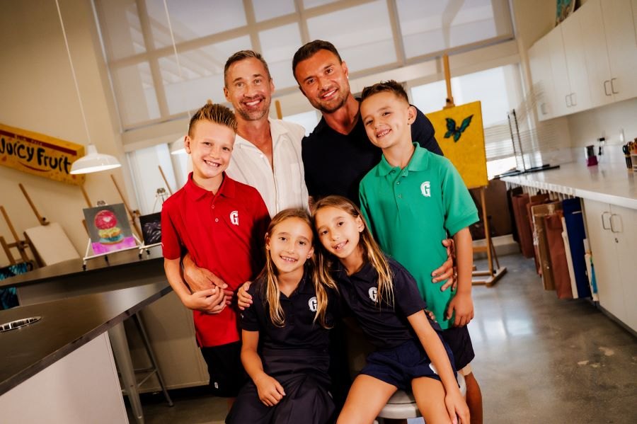 Two adults and four children in school uniforms pose together in an art classroom.