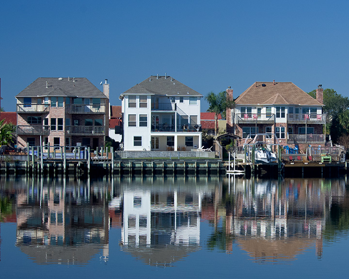 Multi-story waterfront homes with private docks reflected in calm lake water.