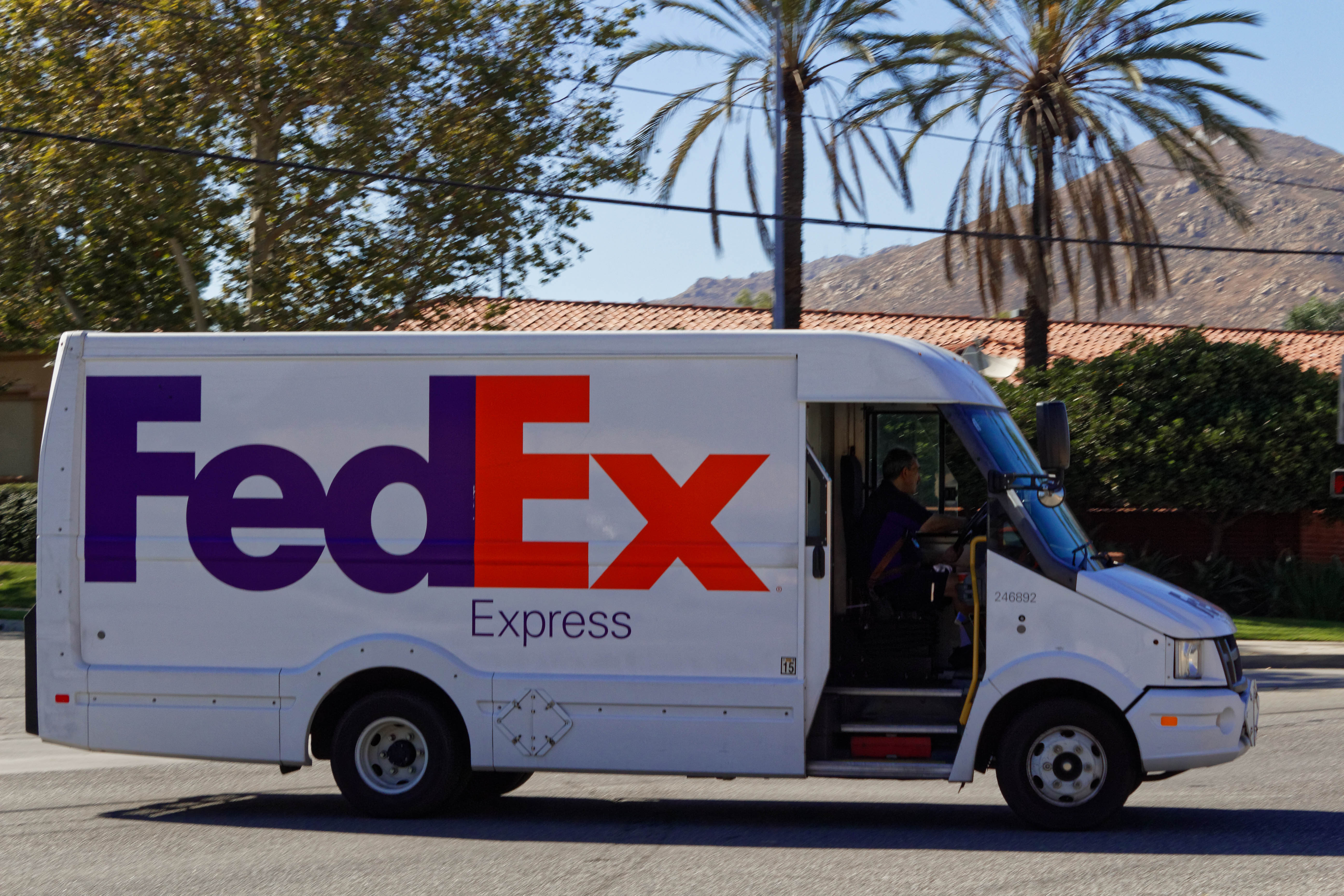 White FedEx Express delivery van with open side door on a palm-lined street