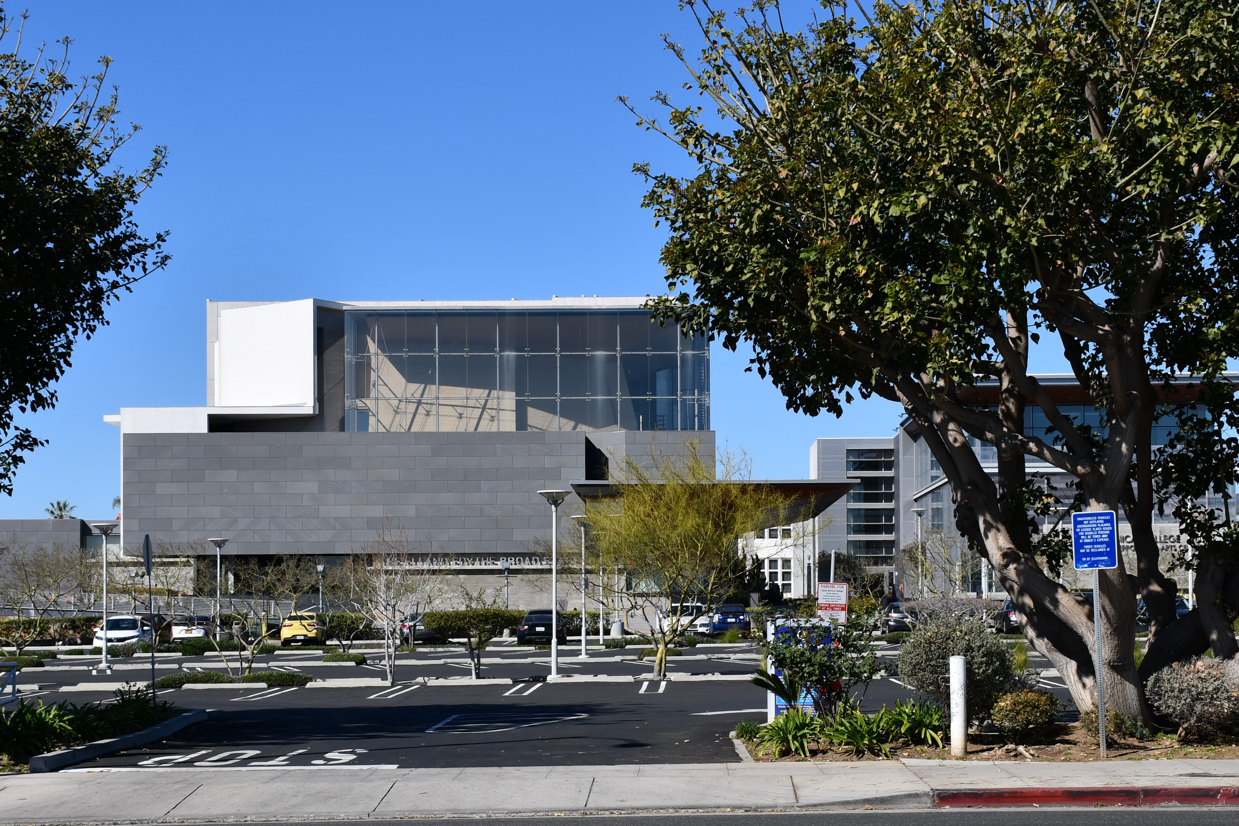 Modern glass and concrete performing arts building exterior under a clear blue sky.