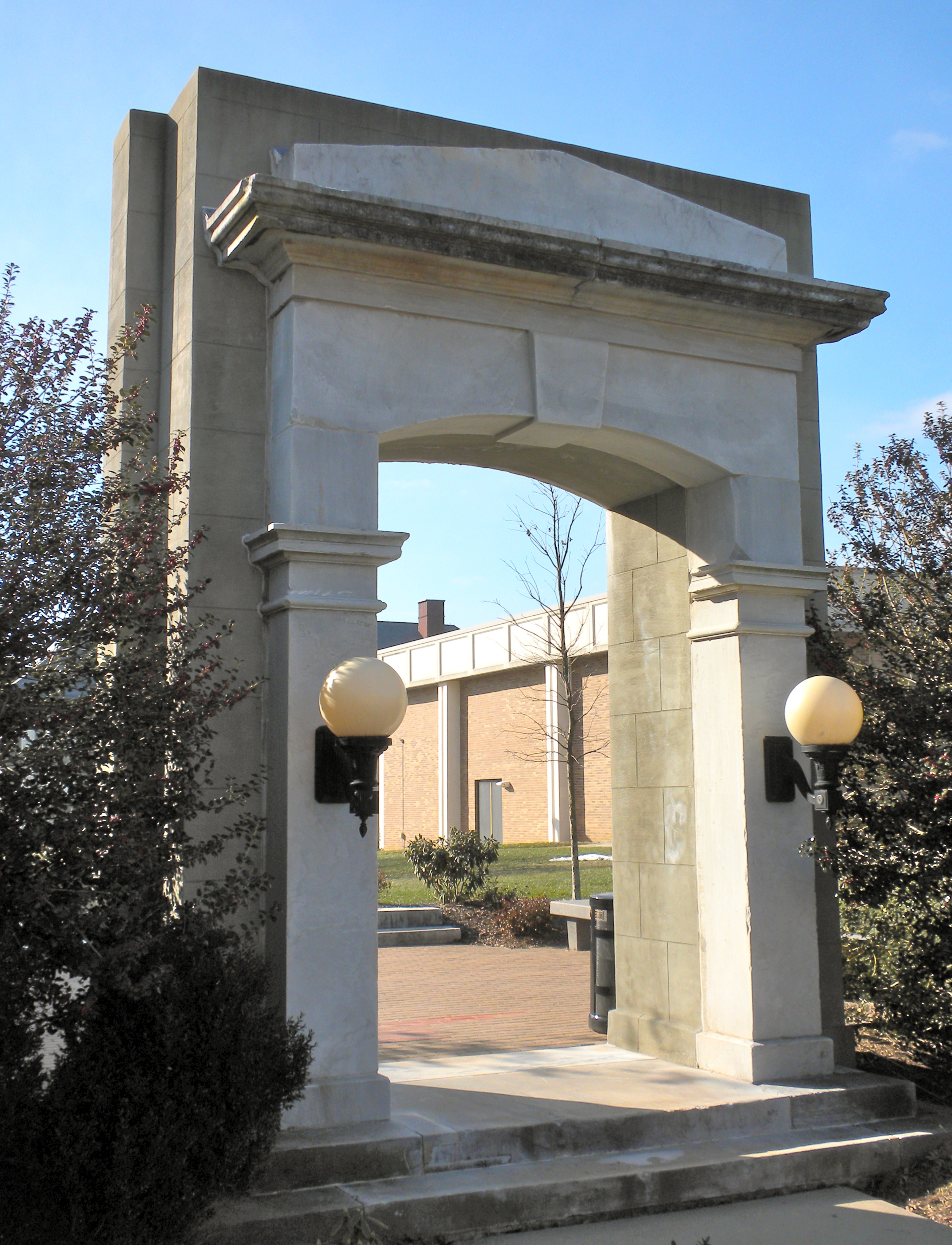 Stone arch gateway leading to a brick walkway on a university campus.