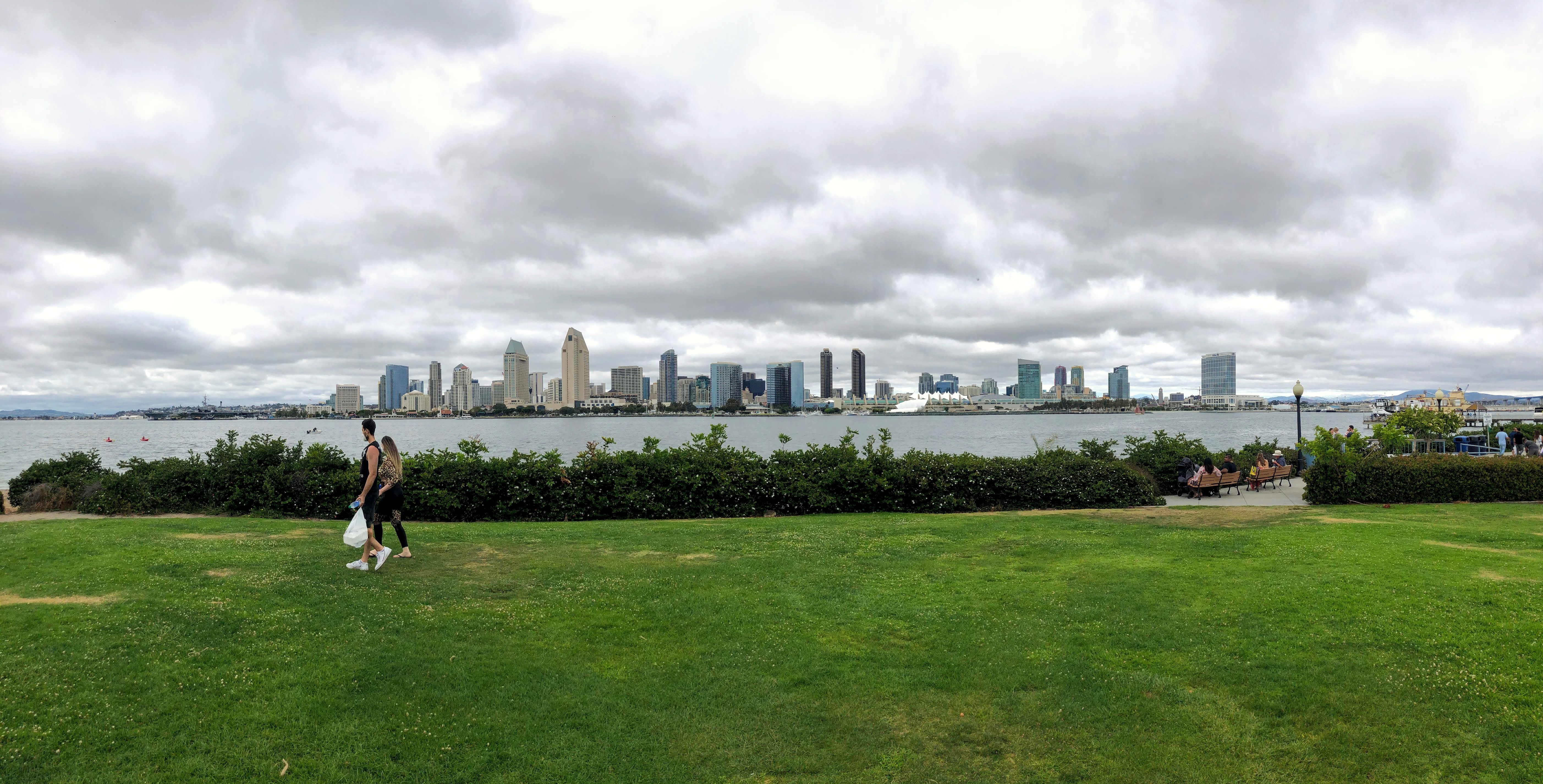 Grassy waterfront park on Coronado with the San Diego skyline visible across the bay under cloudy skies.