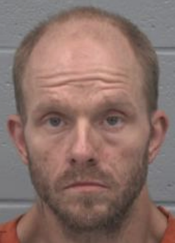 Law enforcement booking photo of a middle-aged man with reddish-blonde hair wearing an orange garment.