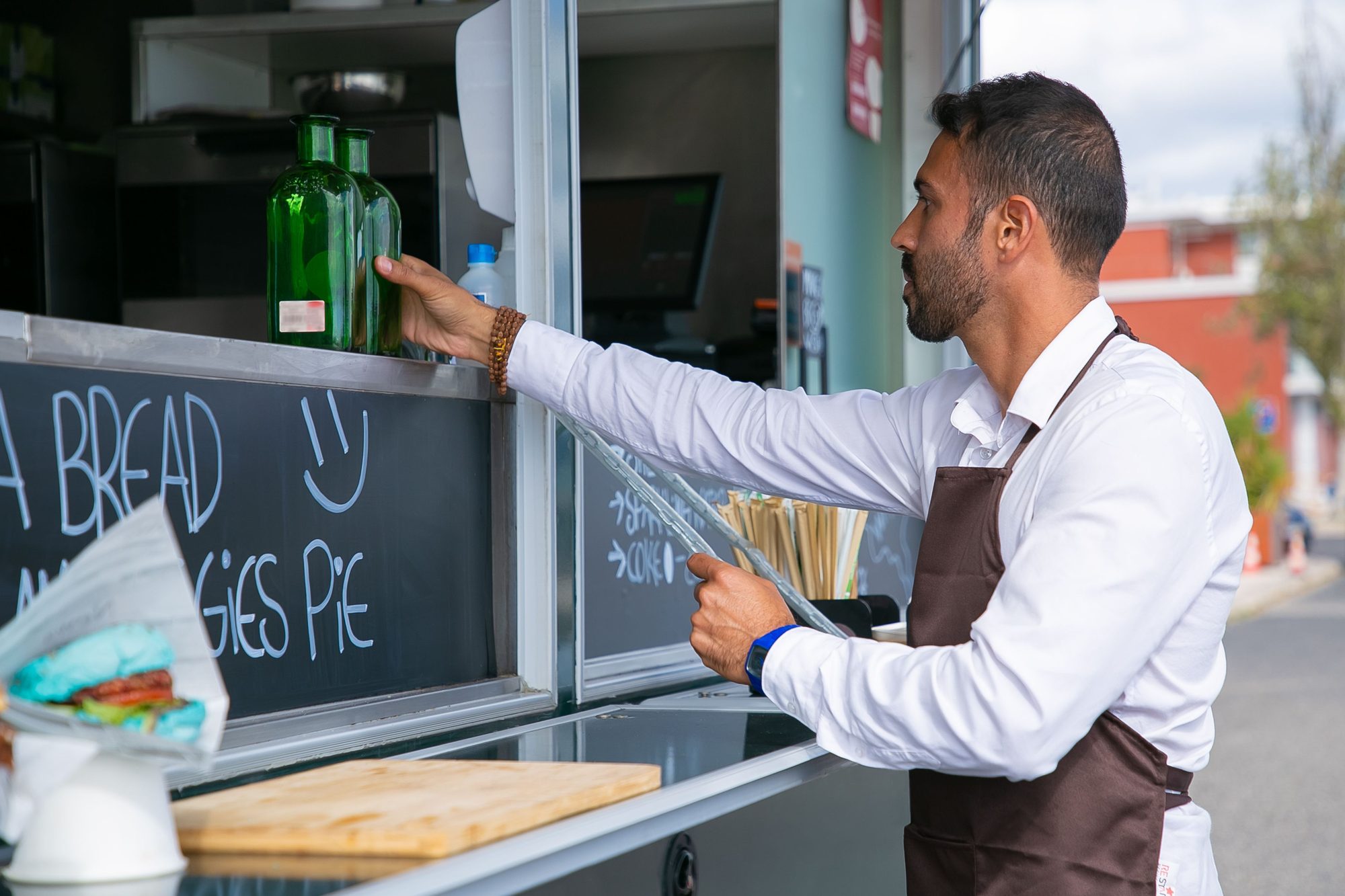 Side view of bearded male seller wearing apron standing near counter of food truck while preparing for job
