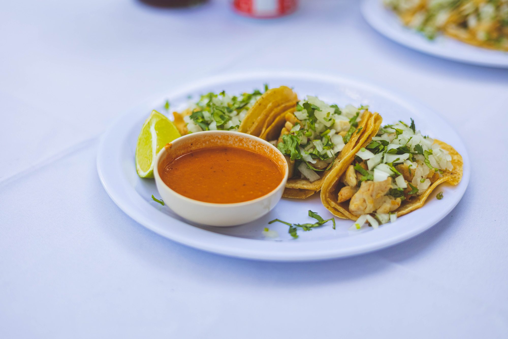 Delicious Mexican tacos on a white plate served with spicy salsa and lime.
