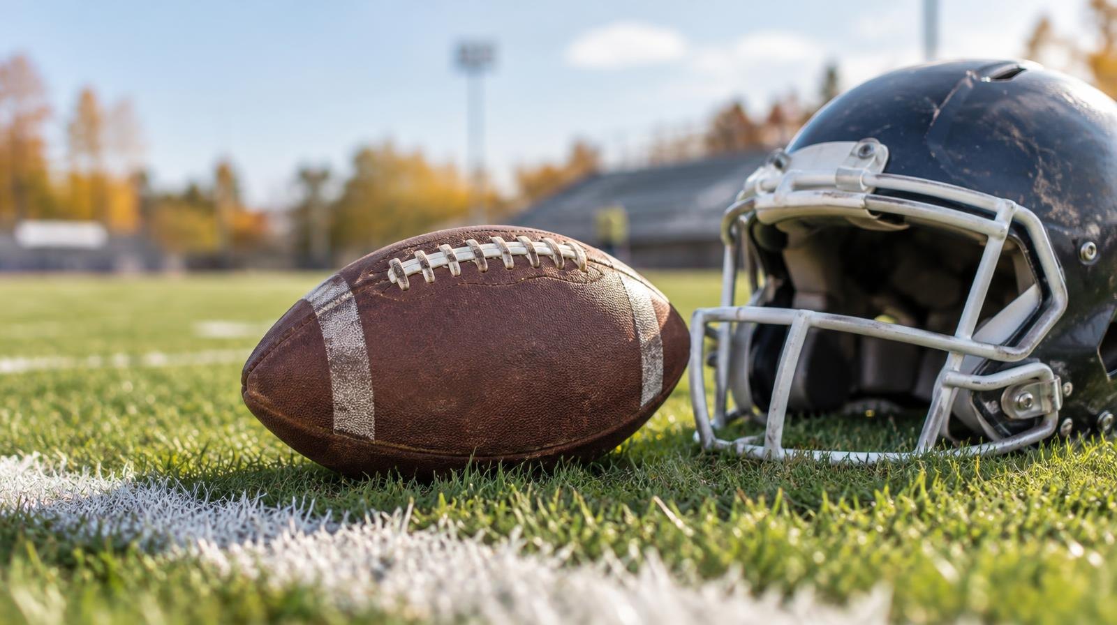 An American football resting on green grass next to a white painted yard line.