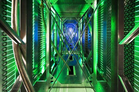 Server racks line a corridor inside a data center, lit by green and blue LEDs.