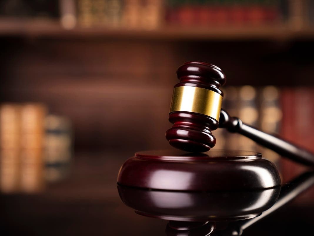 A wooden judge's gavel resting on a sound block with law books in the background.