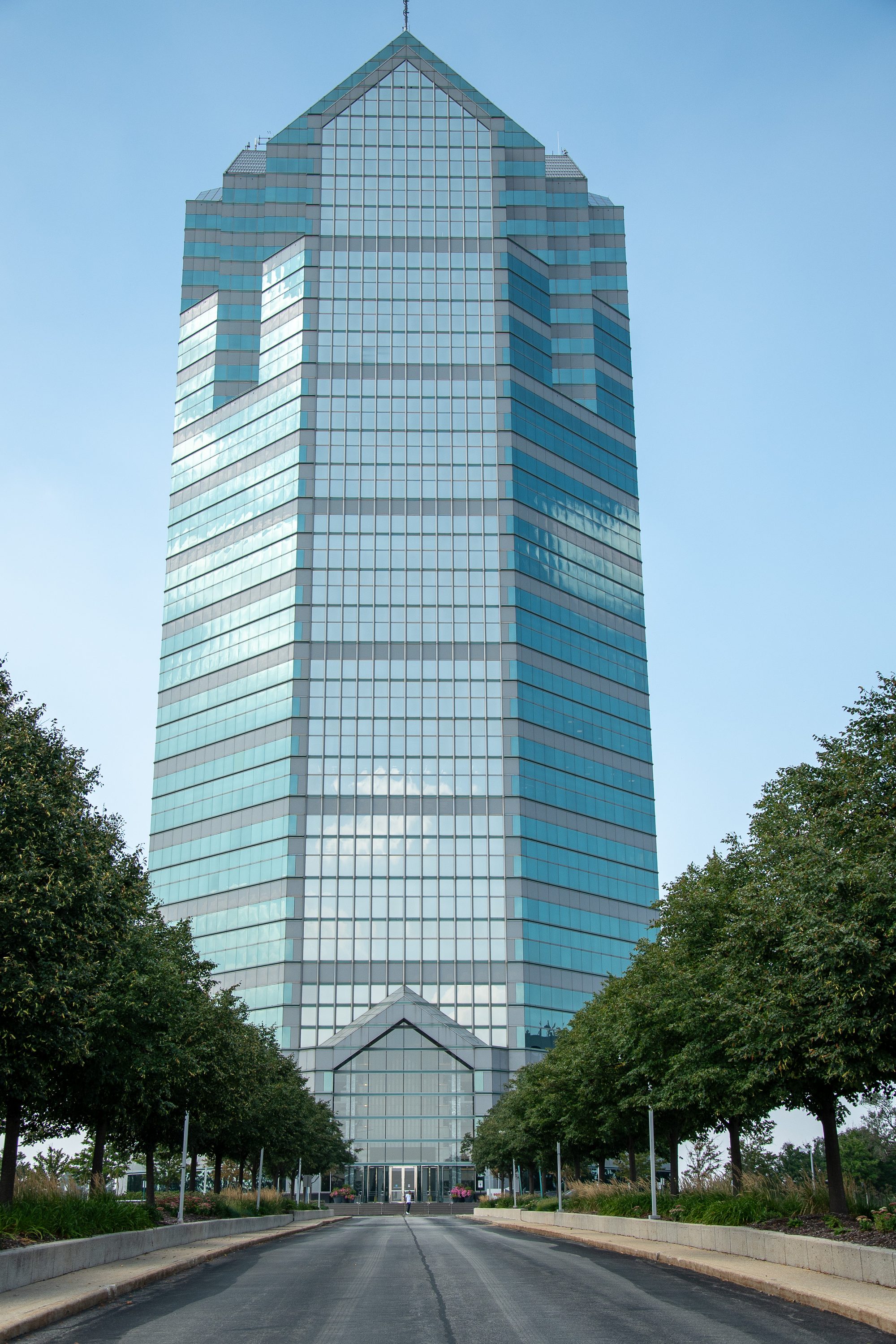 Tall glass office high-rise building and surrounding grounds on a clear day.
