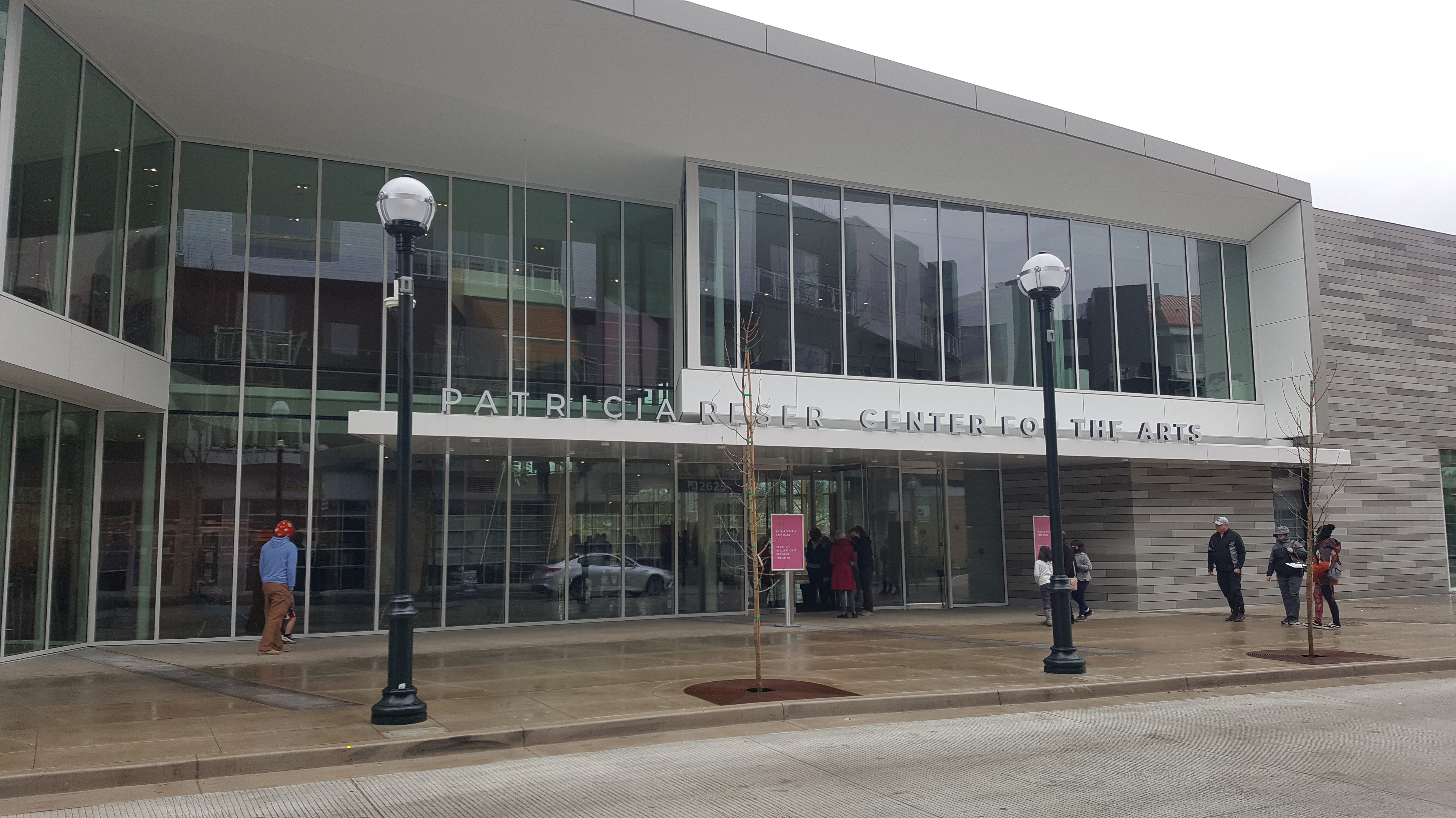 Modern glass-fronted performing arts center exterior with people walking near the entrance.
