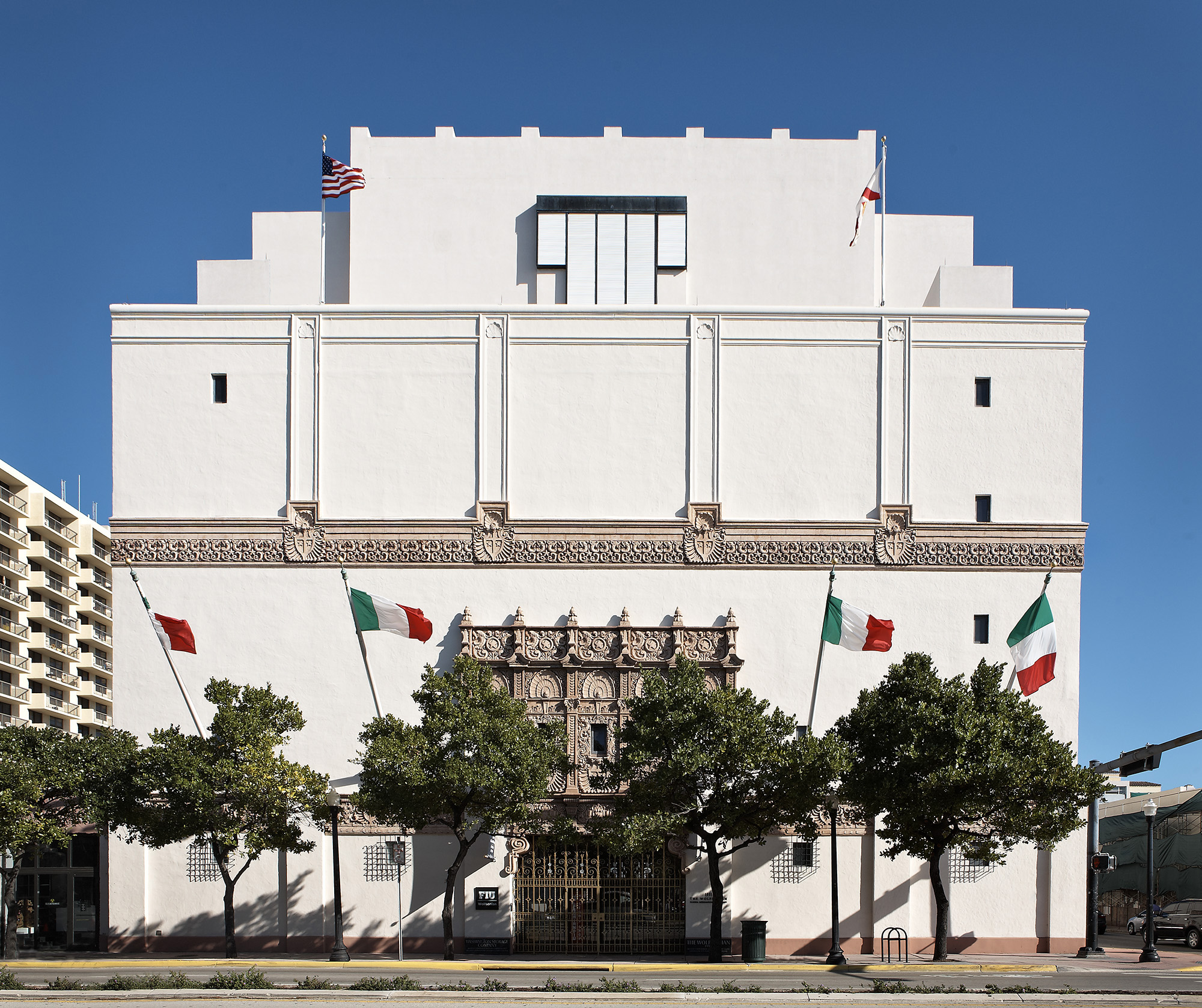 White Mediterranean Revival museum building with ornate entrance and trees along the sidewalk.