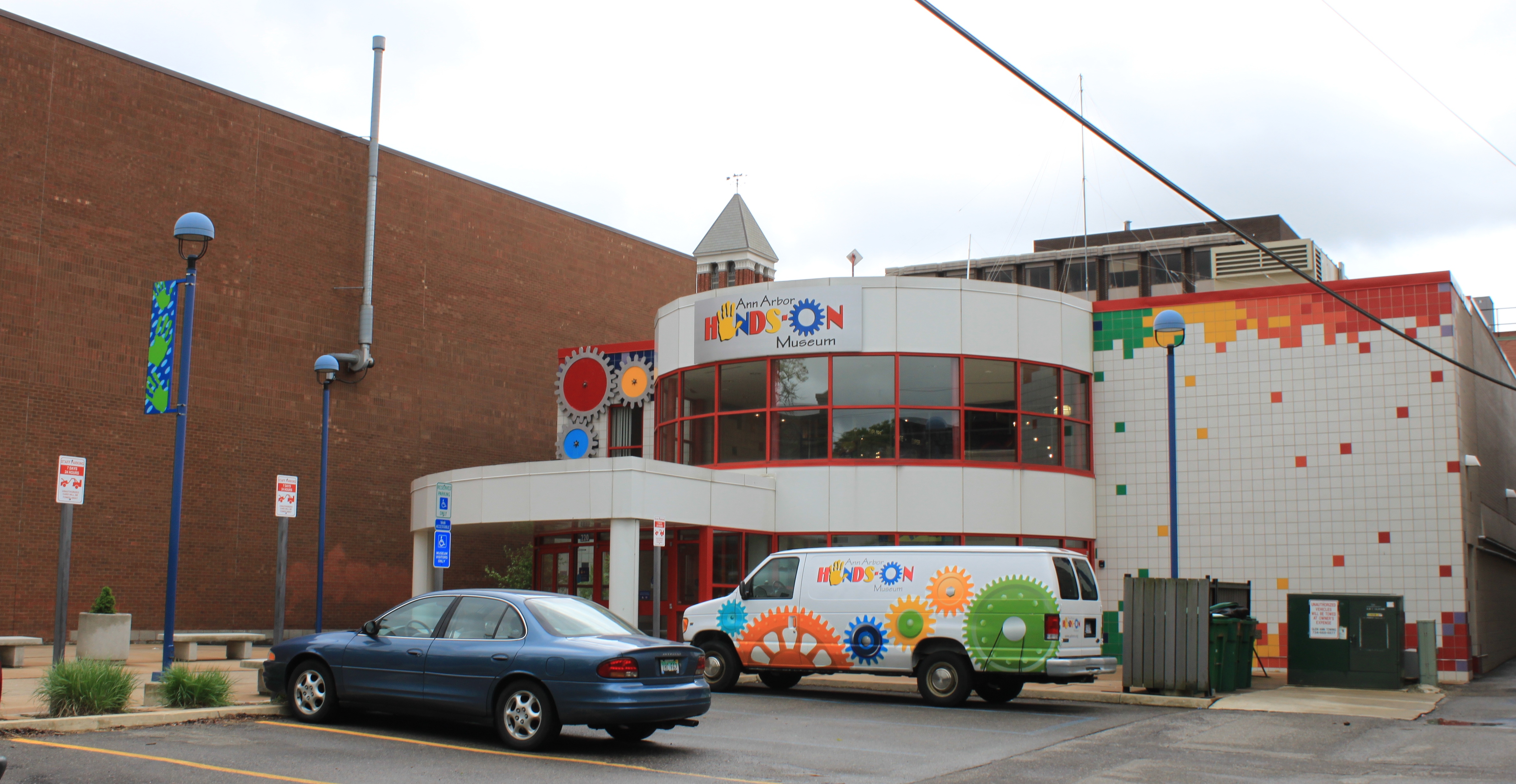 Curved white museum entrance facade with colorful signage and a branded van in the parking lot.