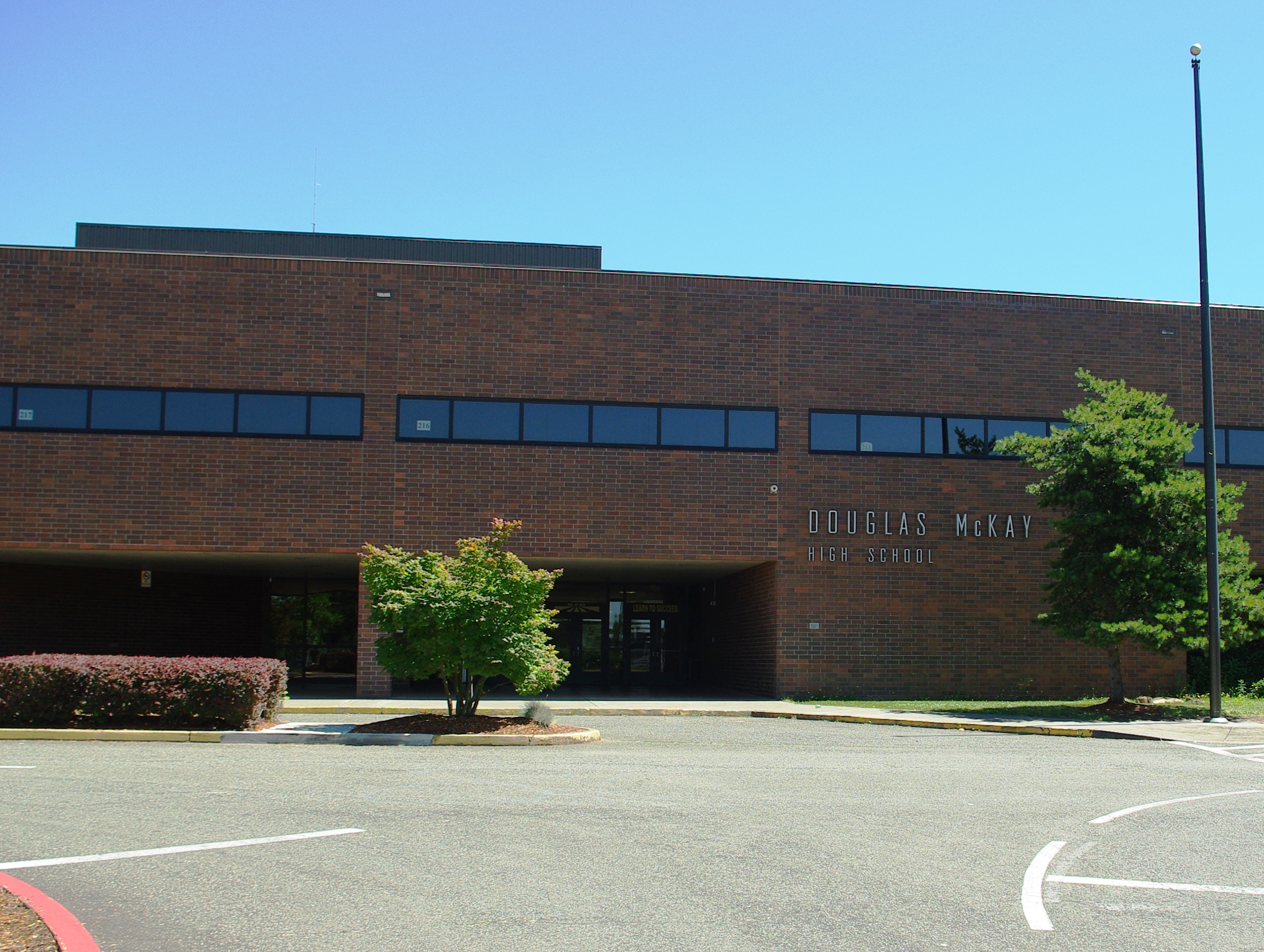 Exterior facade of a two-story brick high school building with large windows and landscaped entrance.