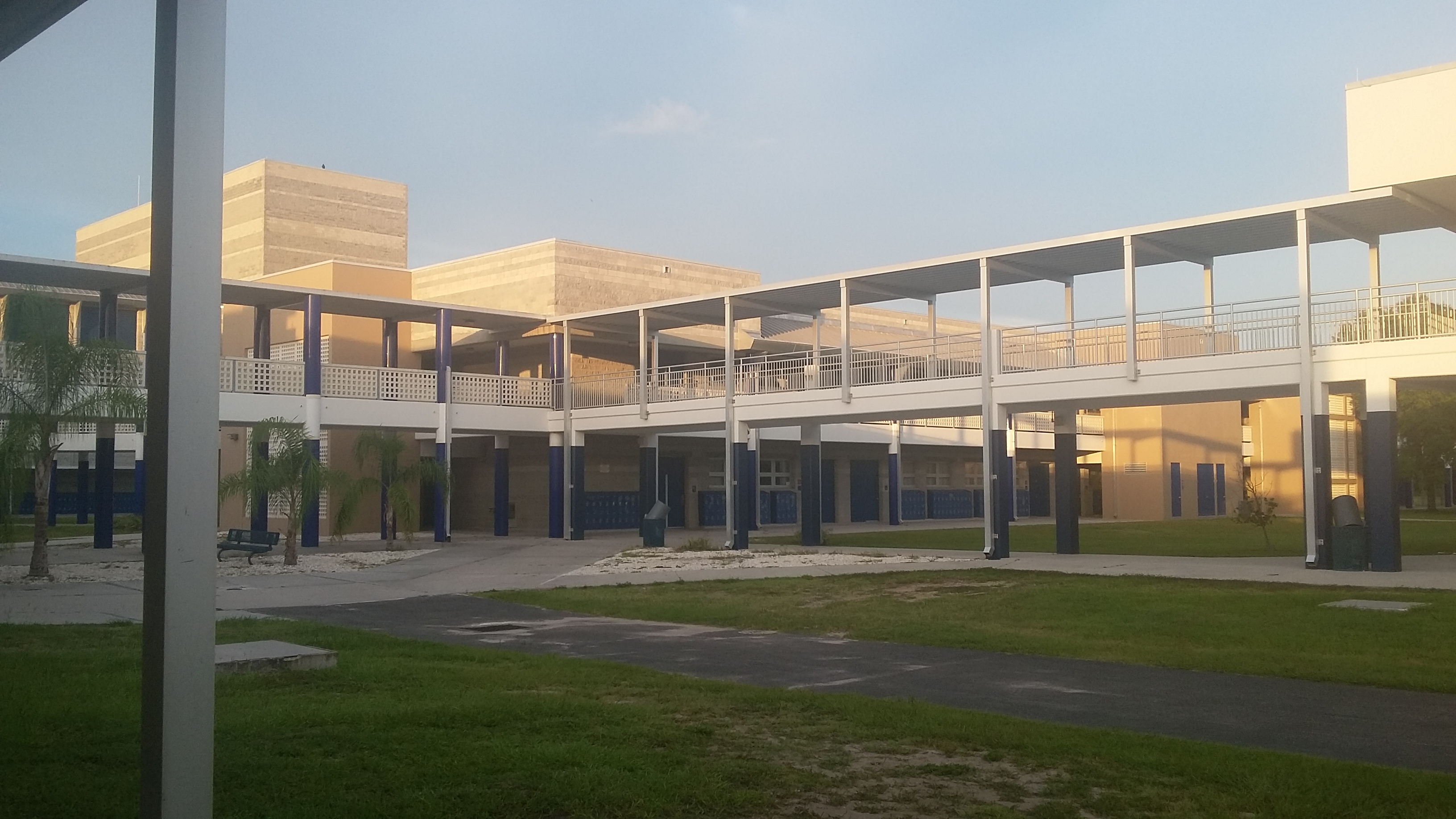 Two-story school campus with open breezeways, covered walkways, and a grassy courtyard.