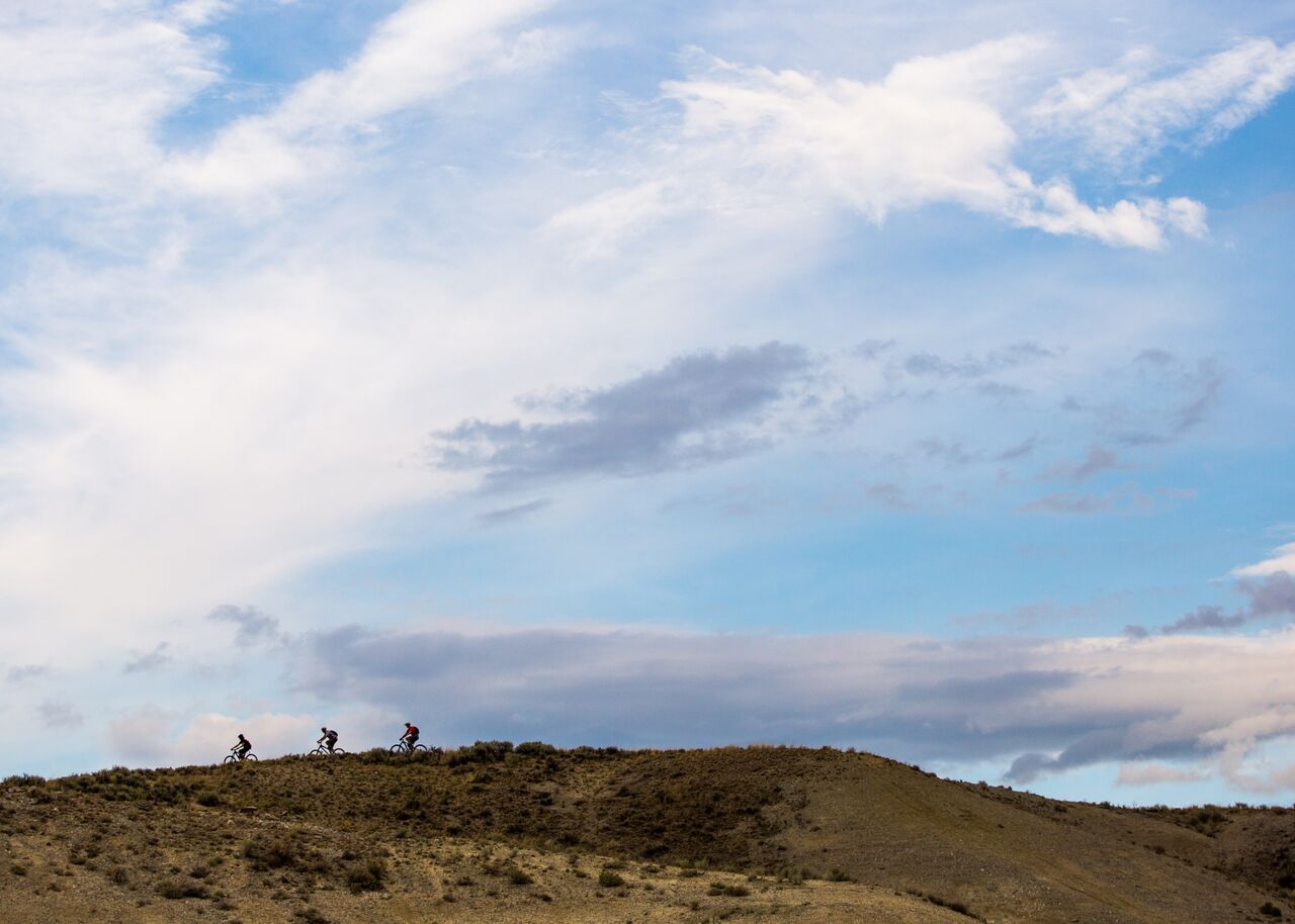 Two mountain bikers silhouetted on a ridgeline against a blue sky.
