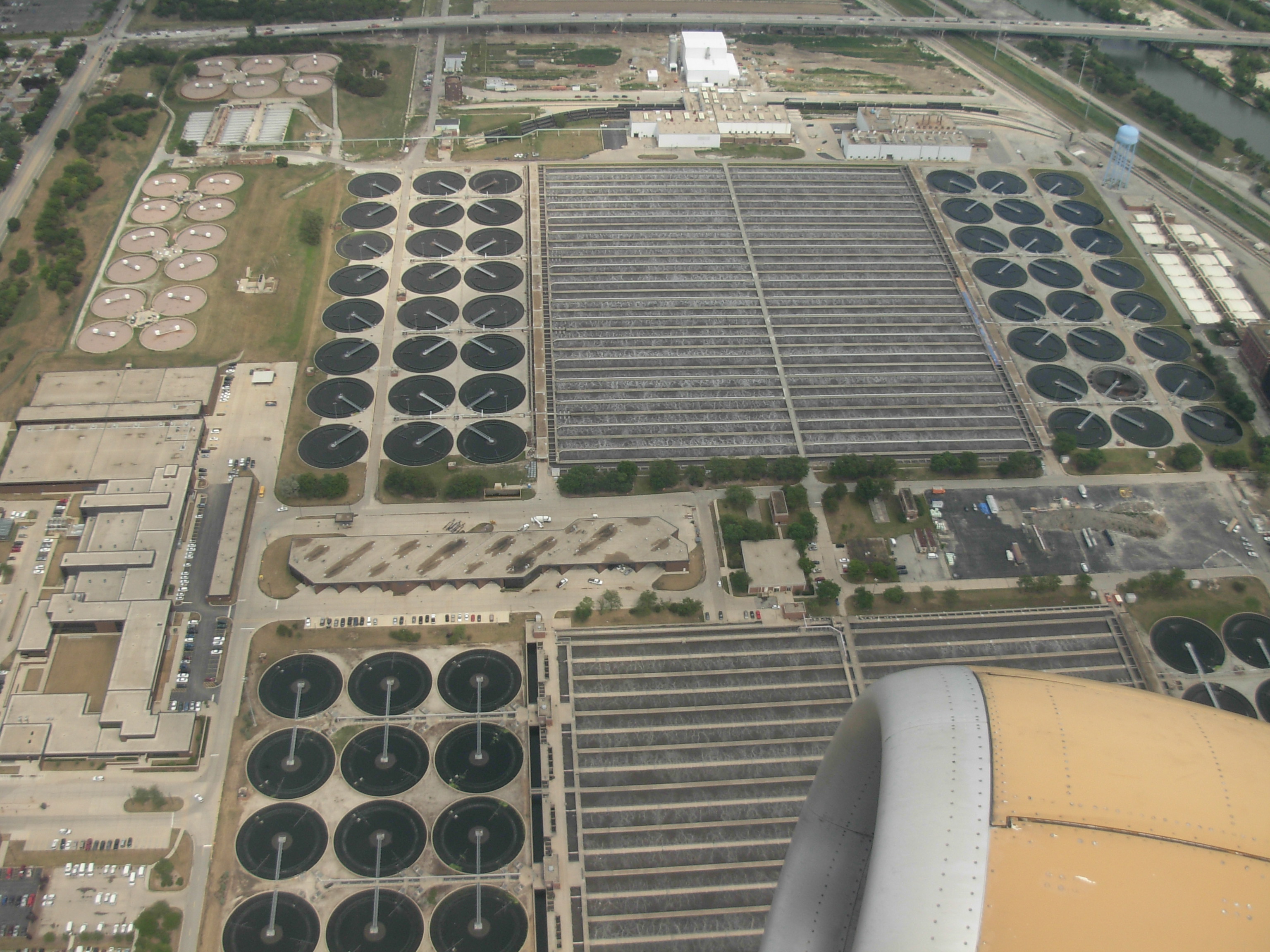 Aerial view of a large wastewater treatment plant with circular clarifier tanks and rectangular filter beds.