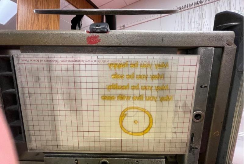 A metal-framed letterpress platen holding a polymer printing plate with backward text, ready for printing.
