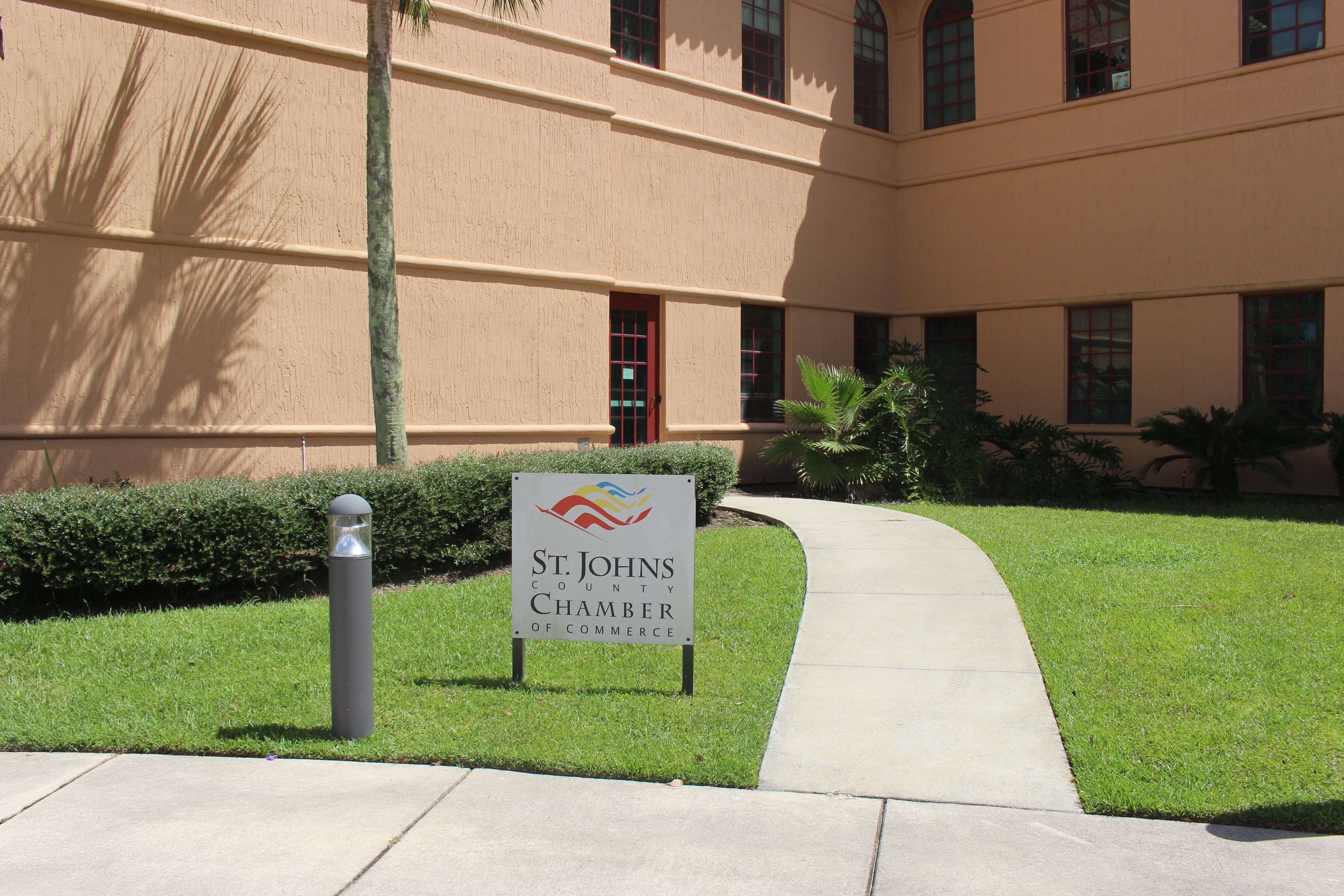Sign for the St. Johns County Chamber of Commerce on a lawn with palm trees.