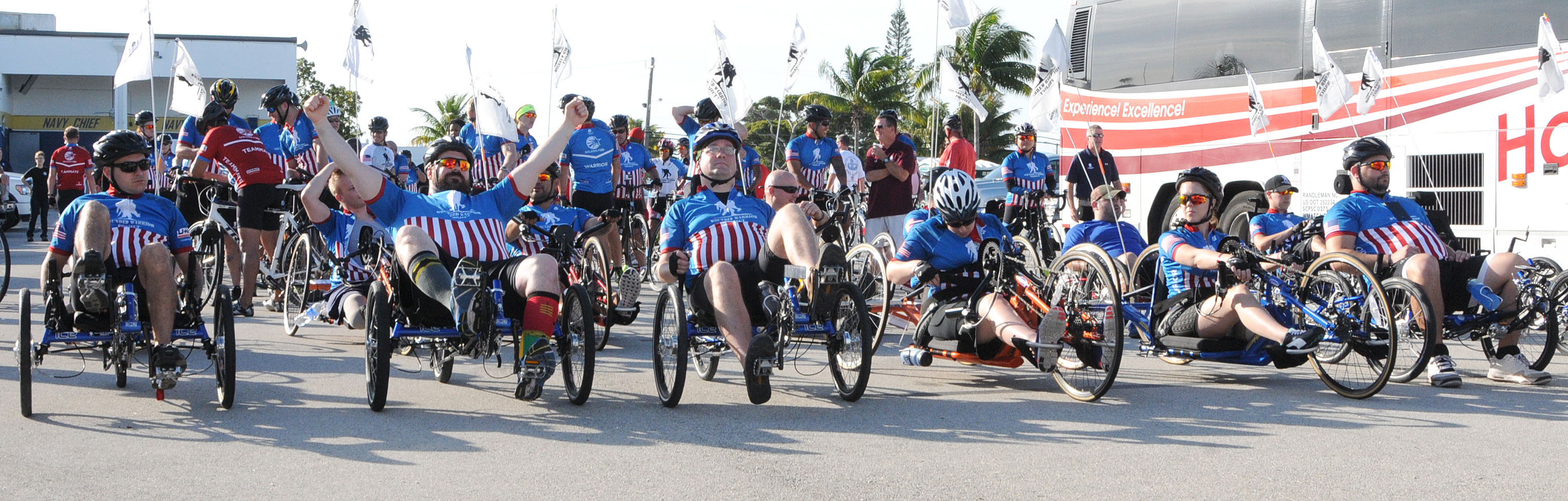 Group of veterans on adaptive hand cycles and recumbent trikes at an outdoor cycling event.