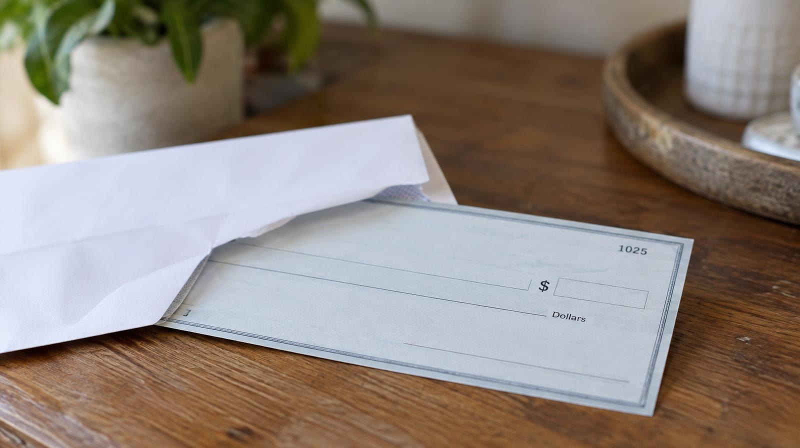 A paper check and white envelope resting on a wooden surface.