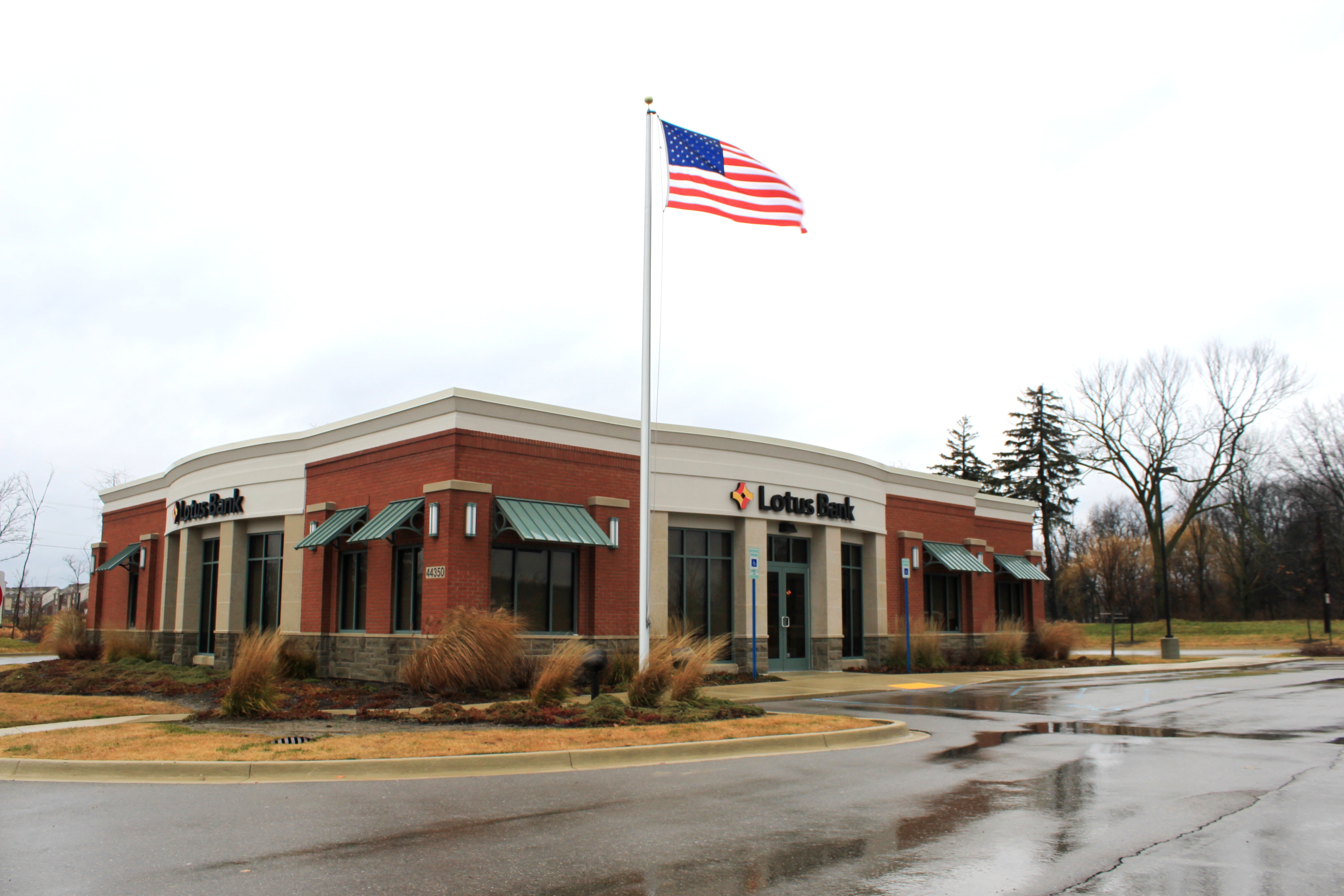 Brick bank building with green awnings and American flag along a Novi road.