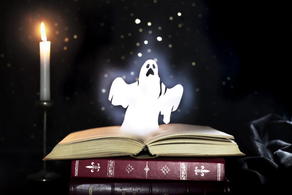 Glowing ghost figure emerging from an open book beside a lit candle on a dark background.