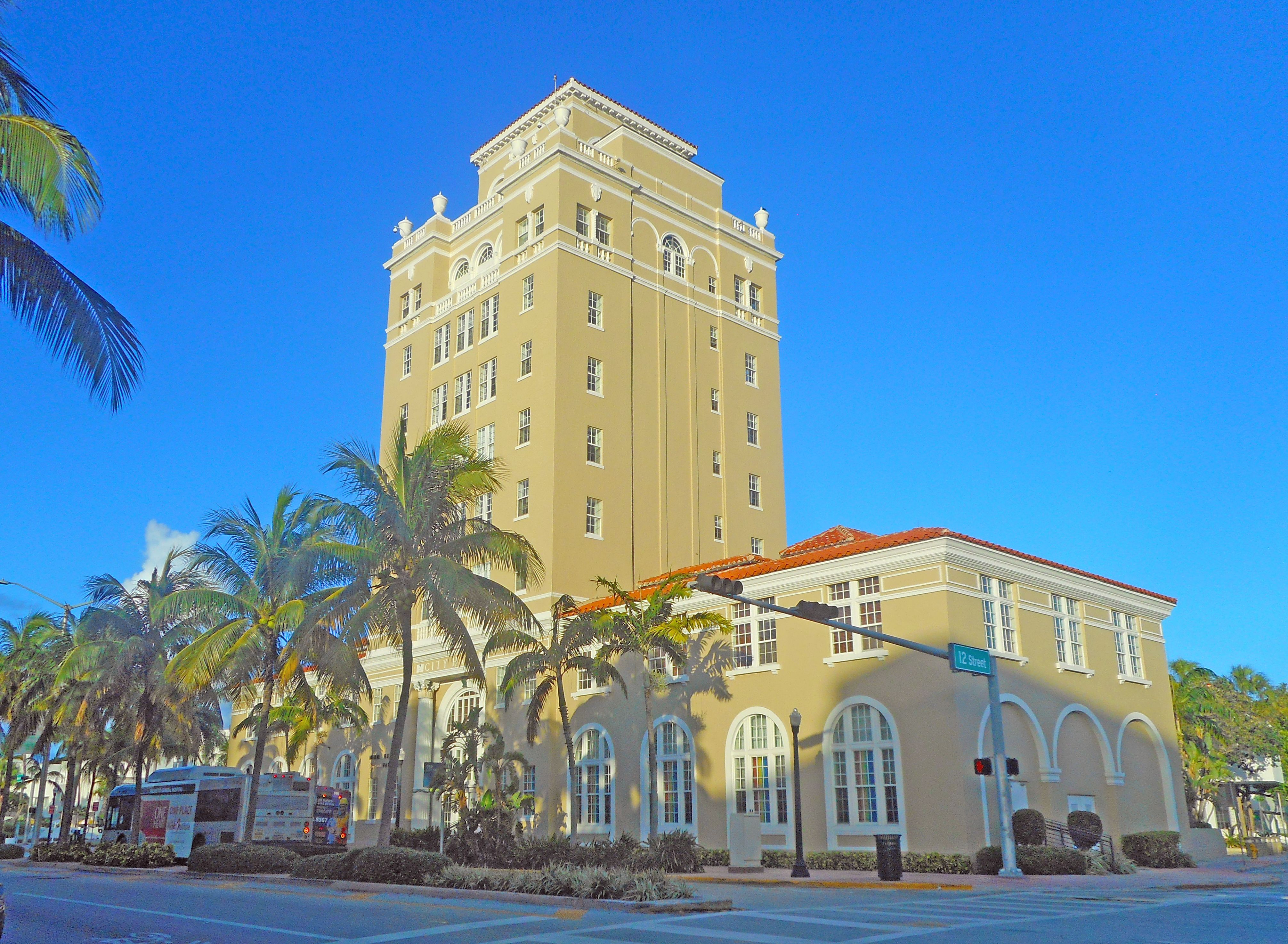 Mediterranean Revival city hall building with a tower and palm trees on a sunny day.