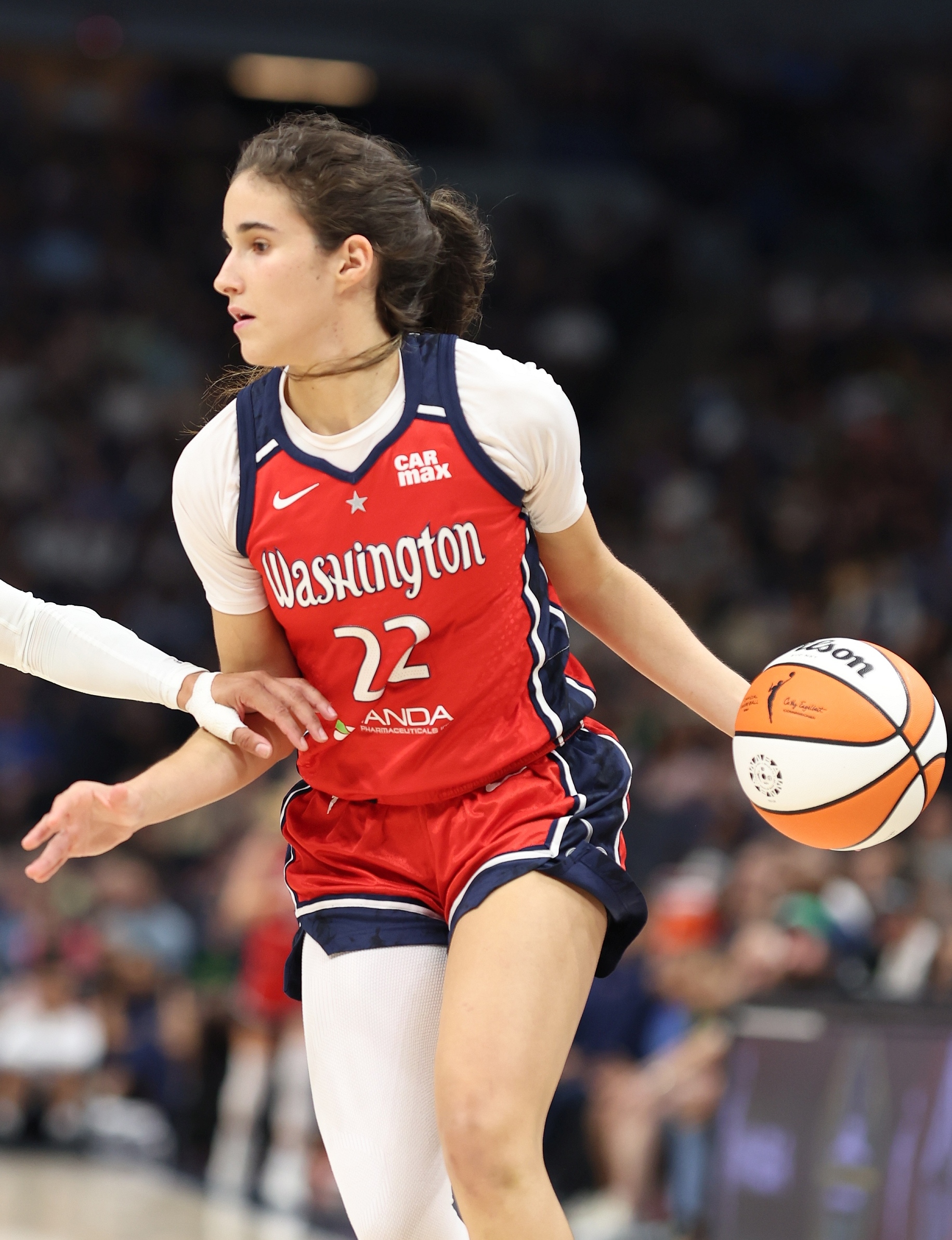 Female basketball player in red Washington Mystics jersey number 22 dribbles a basketball.