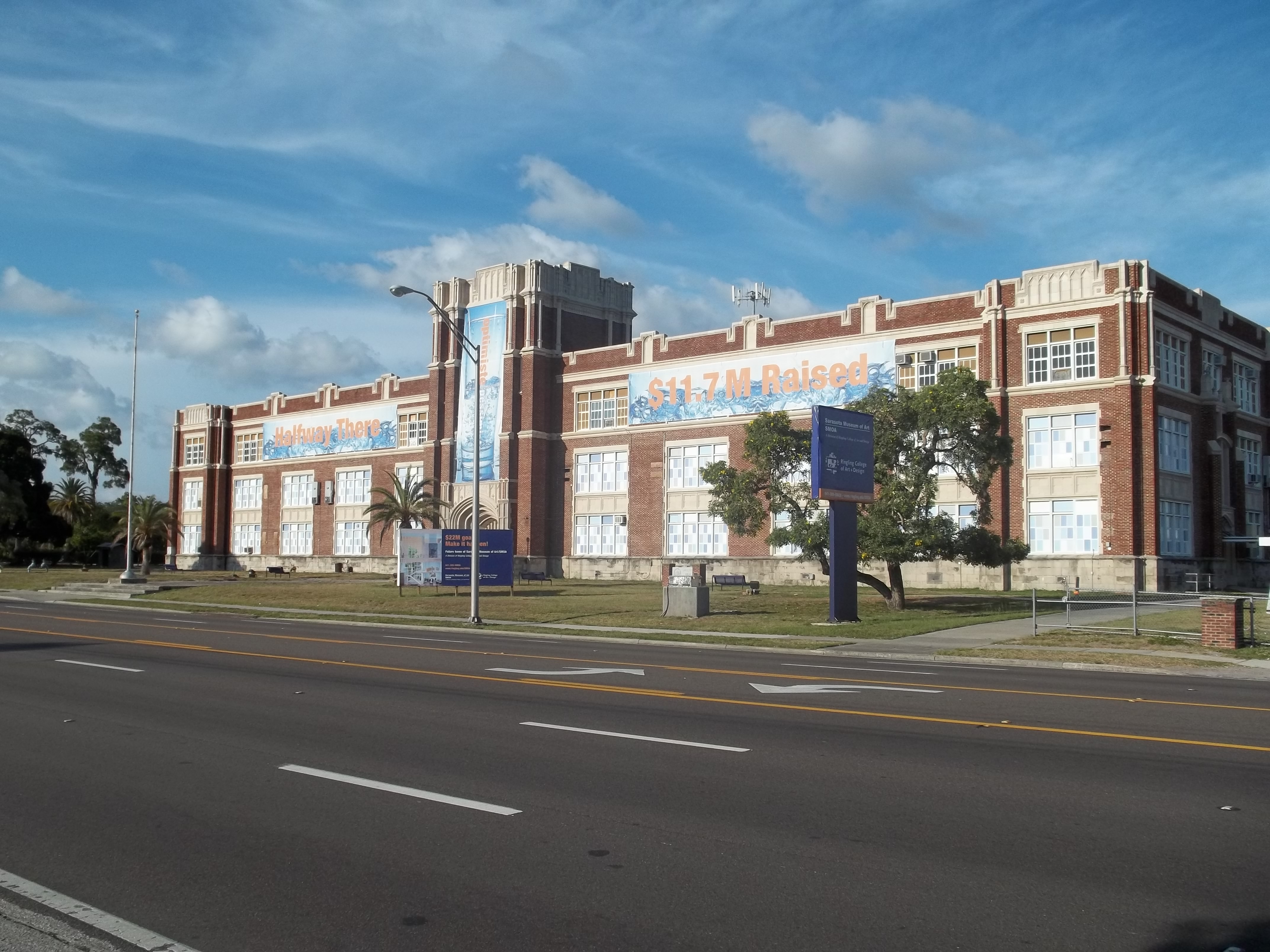 Large red-brick school building with banners and palm trees out front.