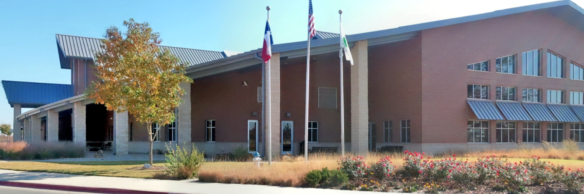 Brick public building with metal roof and three flagpoles in front.