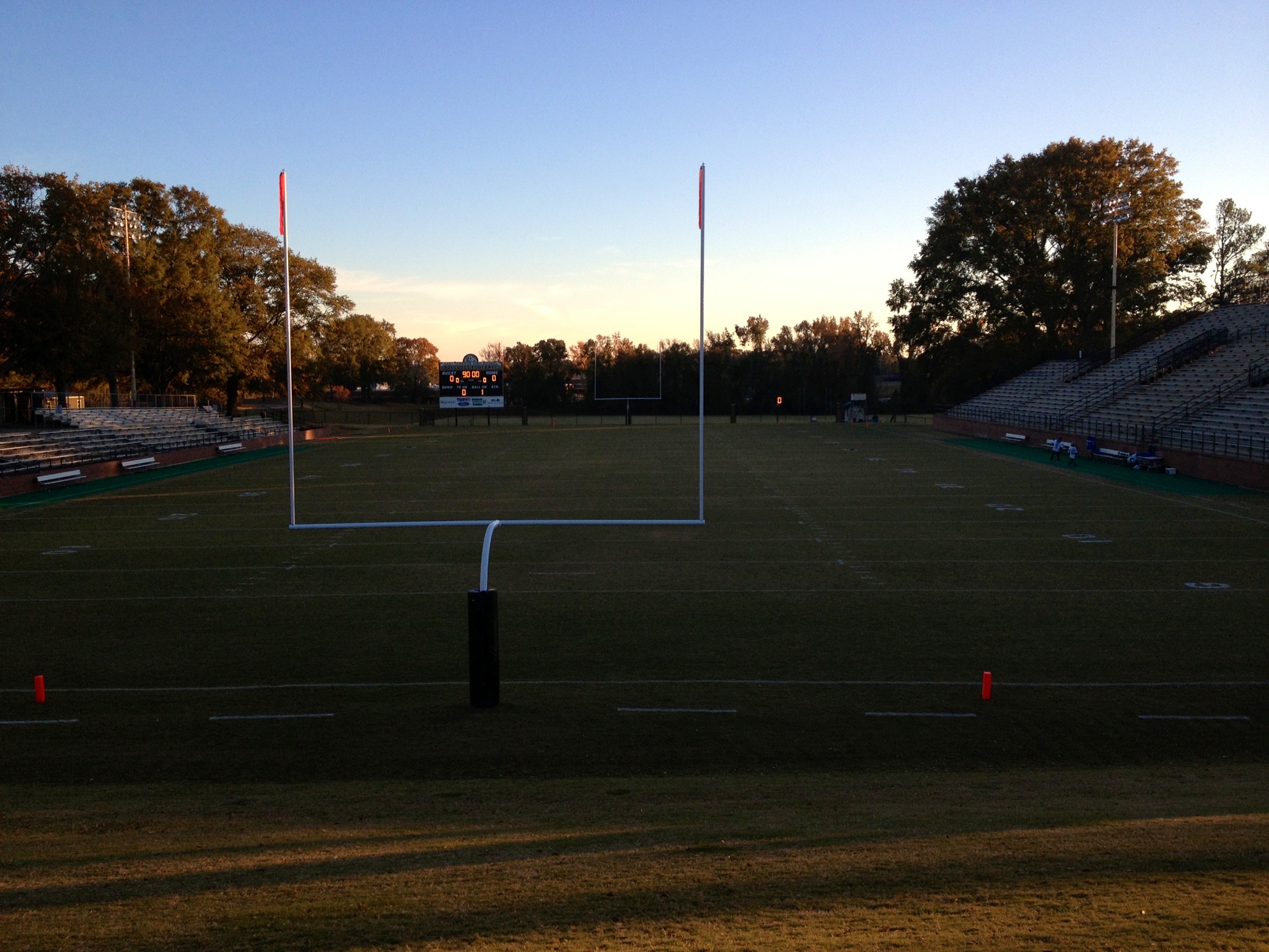 Empty high school football field at dusk with goal posts and bleachers on both sides.