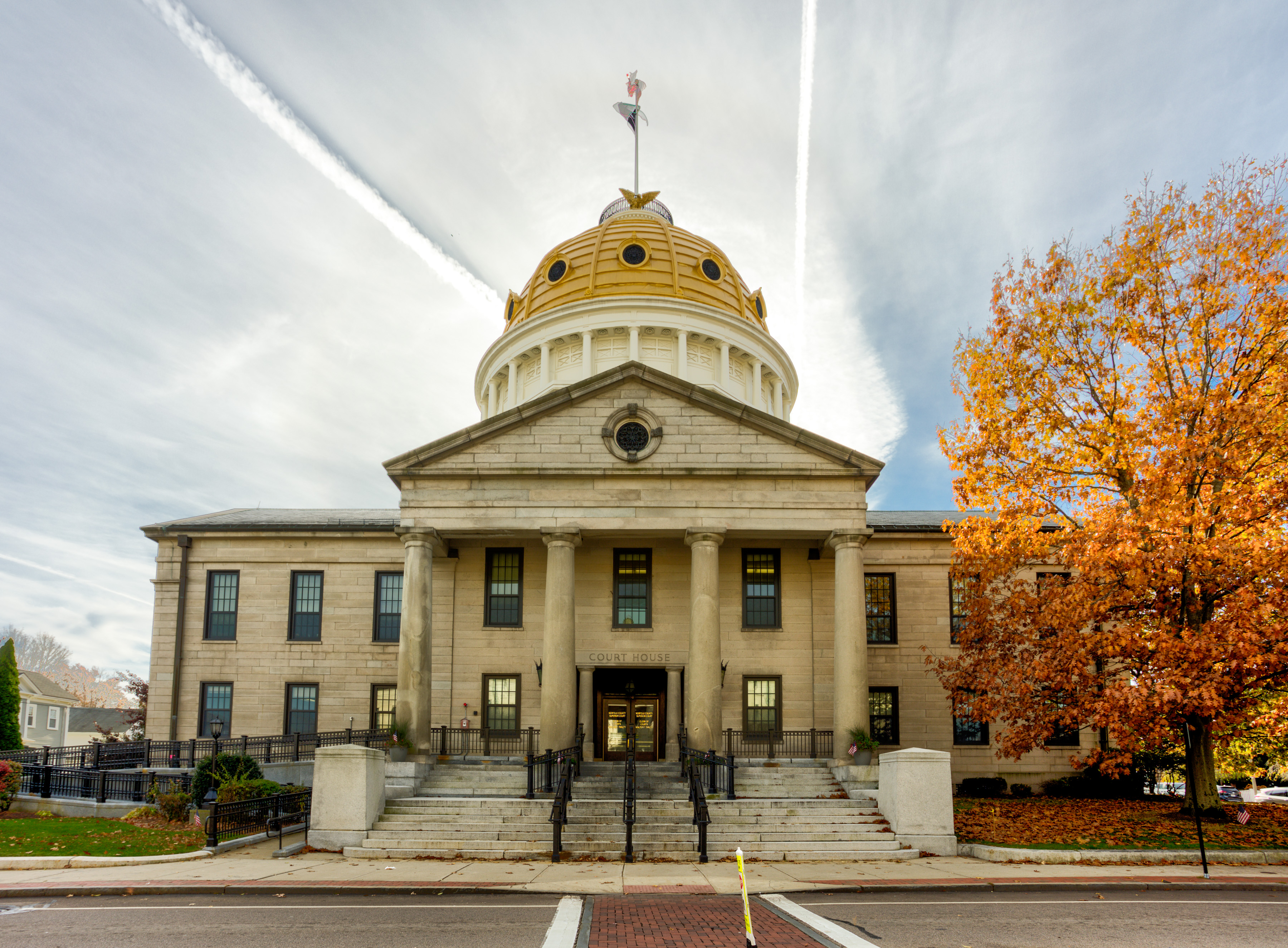 Neoclassical government building with a gold dome and columns, flanked by autumn foliage trees.