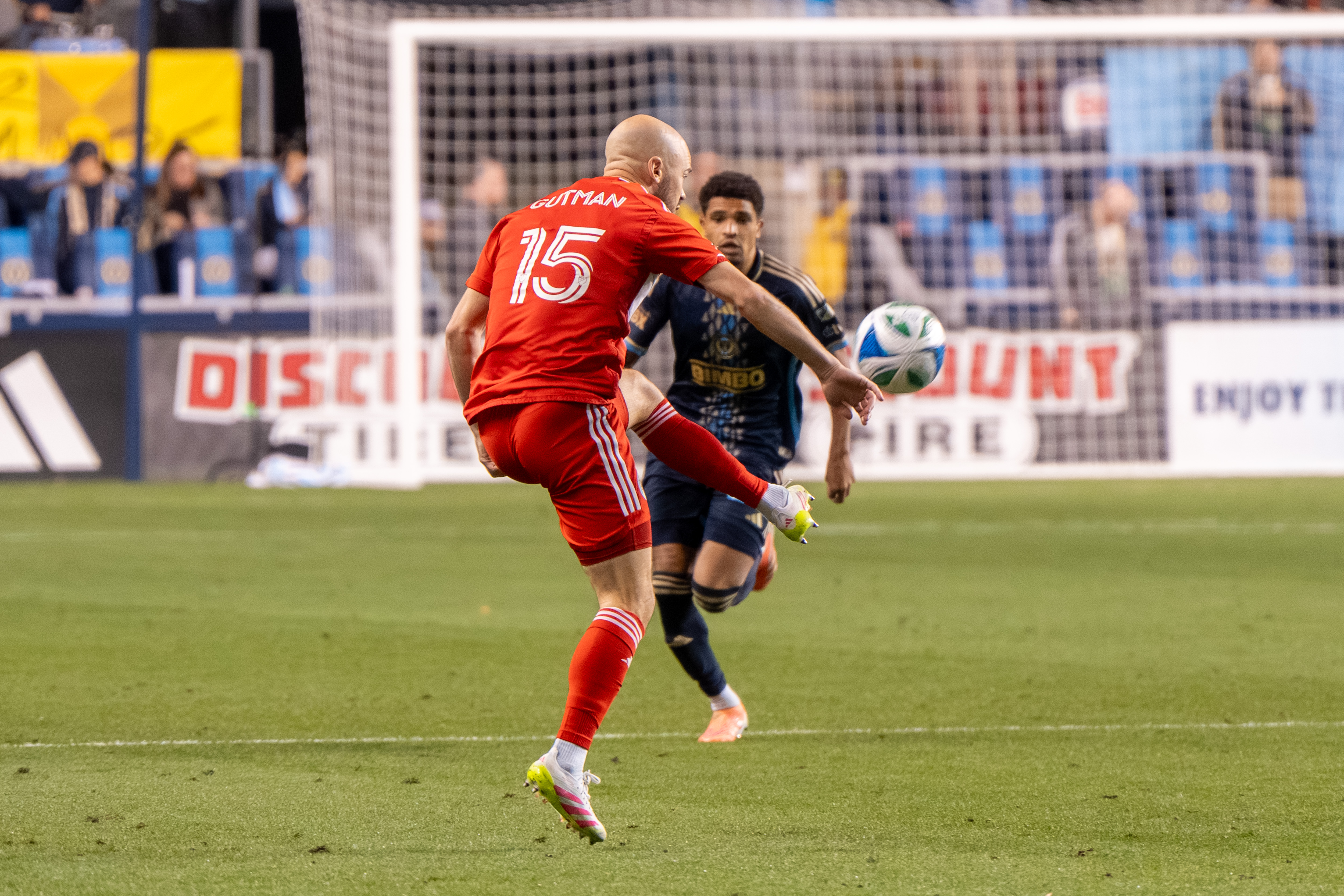 Soccer player in red jersey number 15 labeled Gutman striking a ball during an MLS match.
