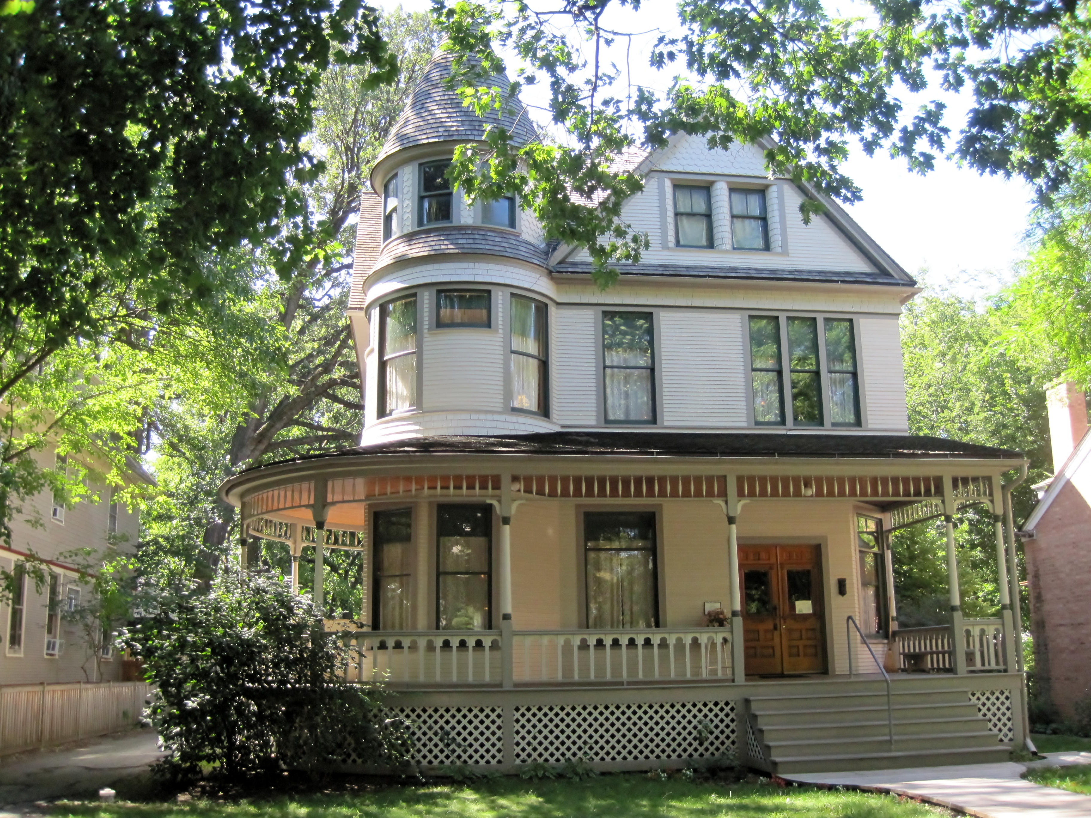 Victorian house with wraparound porch, turret, and bay windows surrounded by trees.
