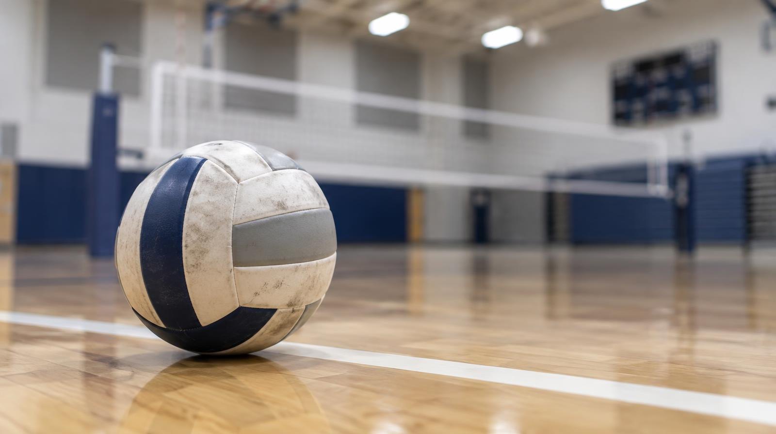 A volleyball resting on a hardwood gym floor near the back boundary line.