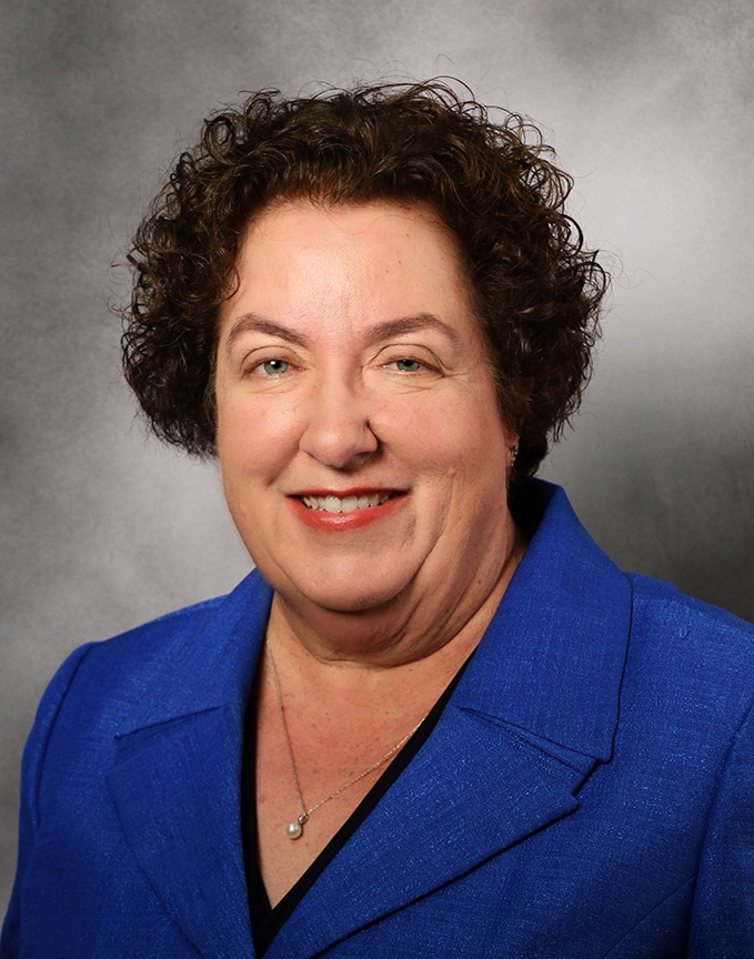 Woman in a blue blazer smiling in a professional headshot against a gray background.