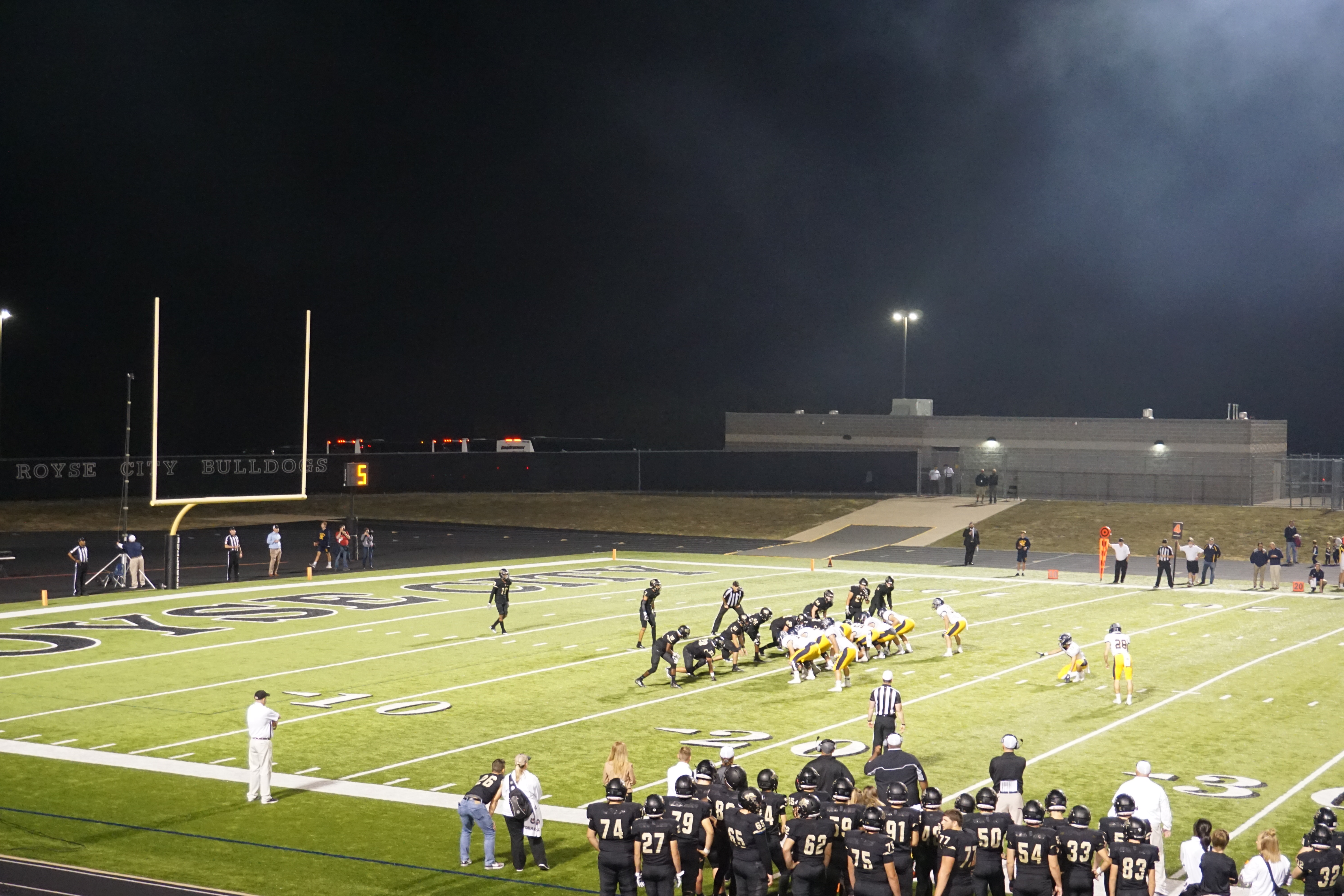 Football players lined up for a field goal attempt under bright stadium lights at night.