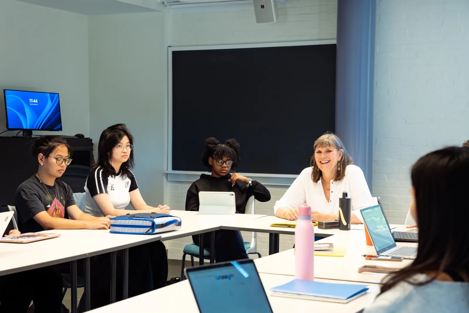 Students seated around a seminar table with laptops and notebooks in a college classroom.