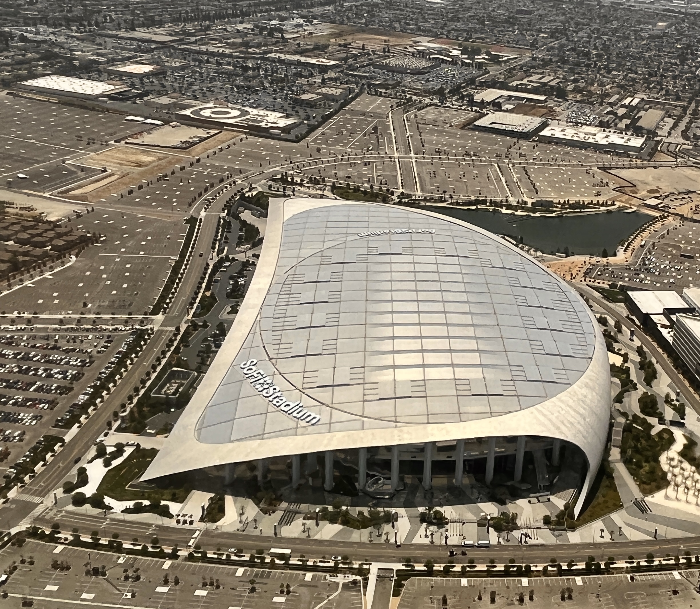 Aerial view of a large stadium with a translucent roof surrounded by parking lots.