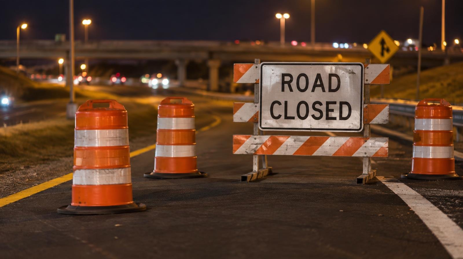 Orange construction barrels blocking a highway on-ramp at night.
