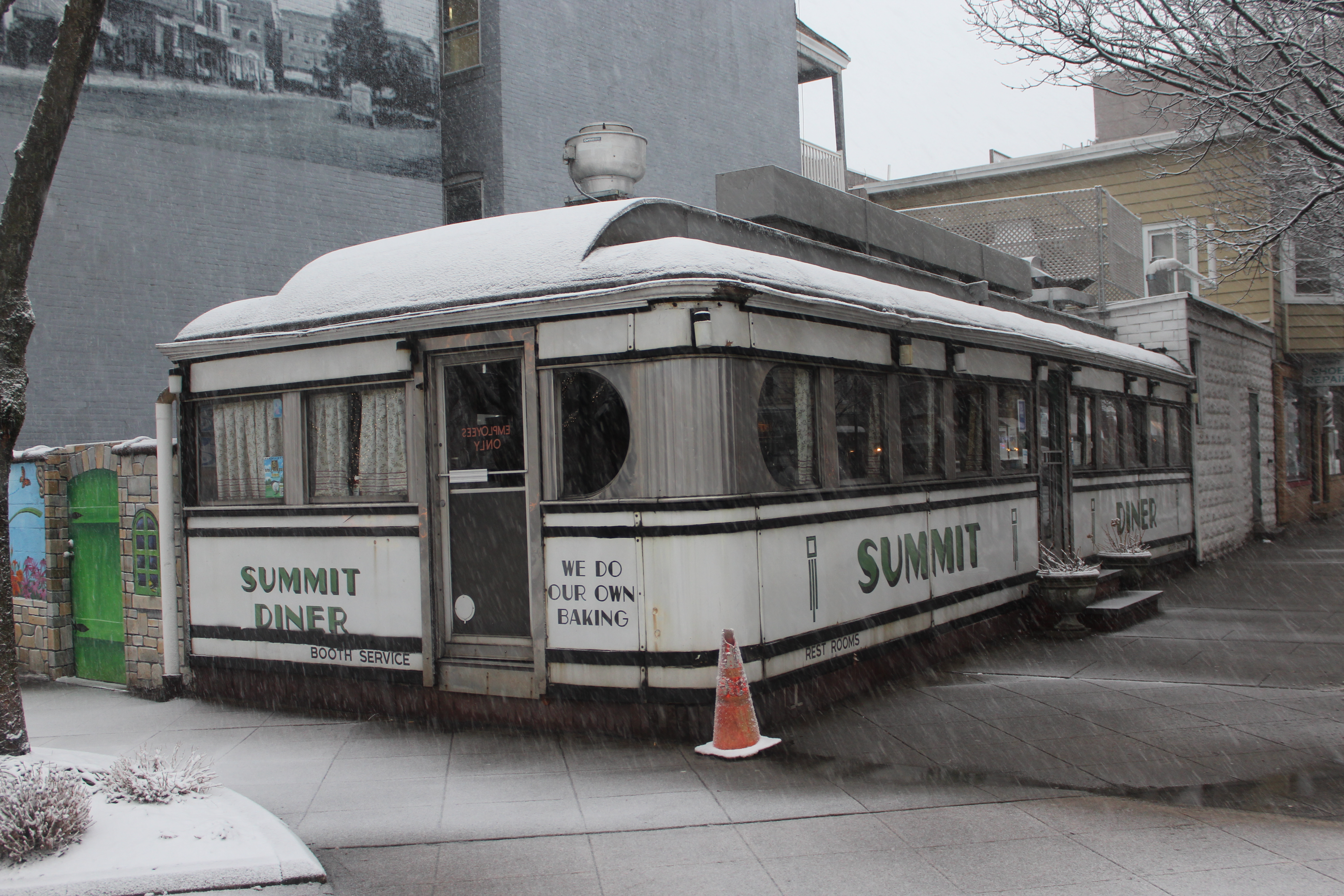 Barrel-roofed stainless-steel diner with green and white signage dusted in snow.