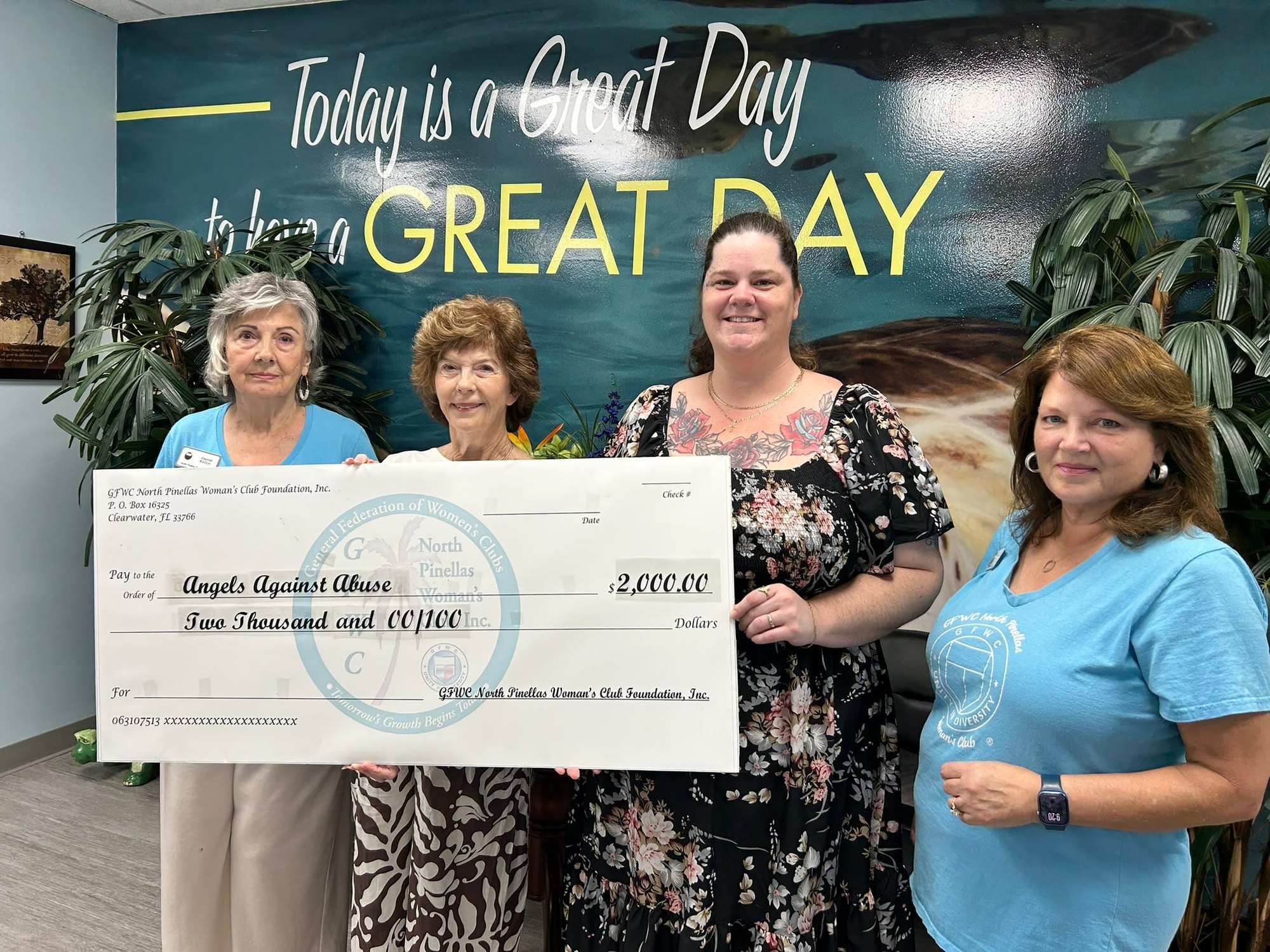 Four women hold a large ceremonial check for two thousand dollars indoors.
