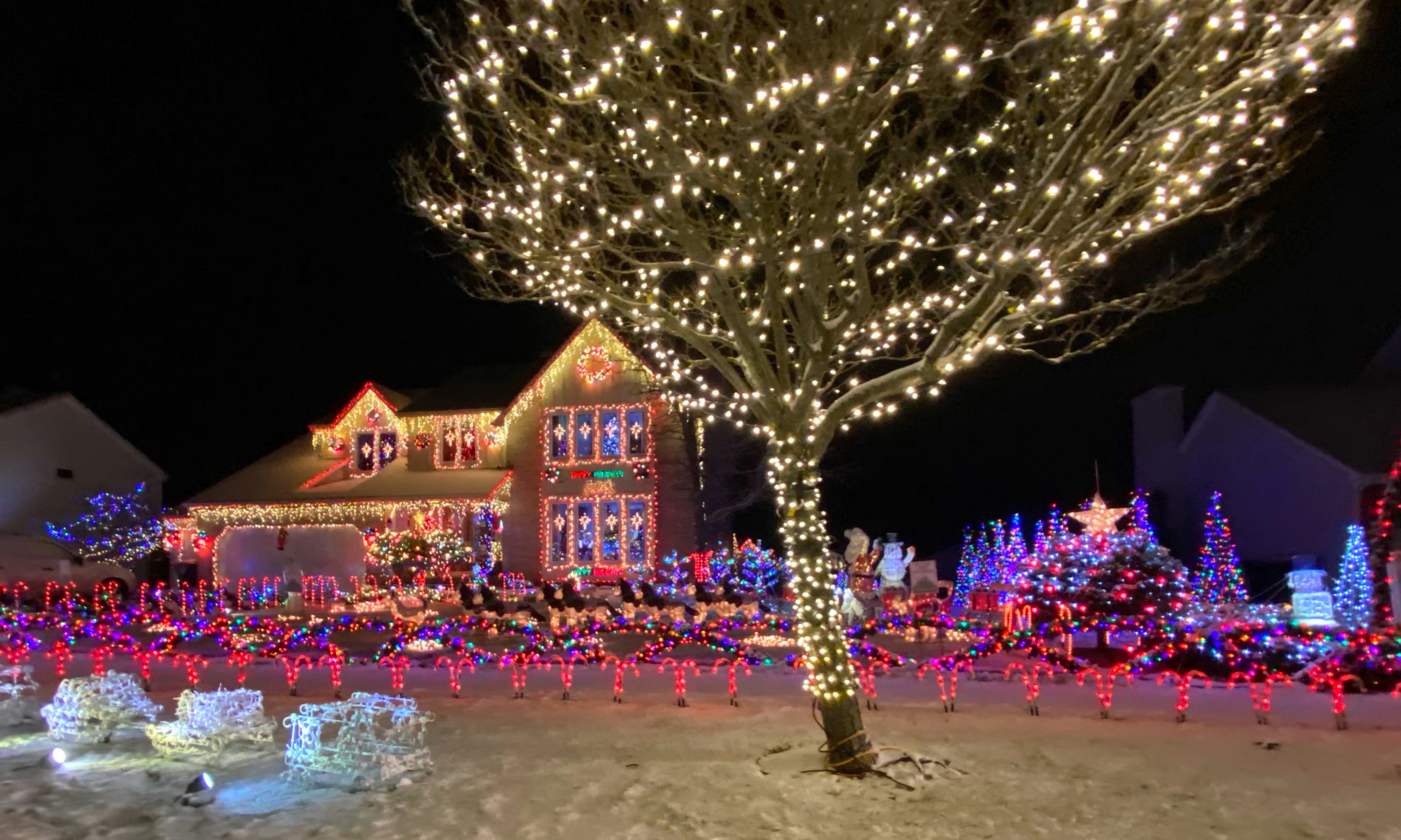 A two-story house covered in colorful Christmas lights glows at night.