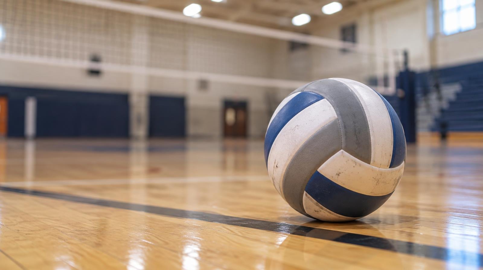 A volleyball resting on a hardwood gym floor near a volleyball net.
